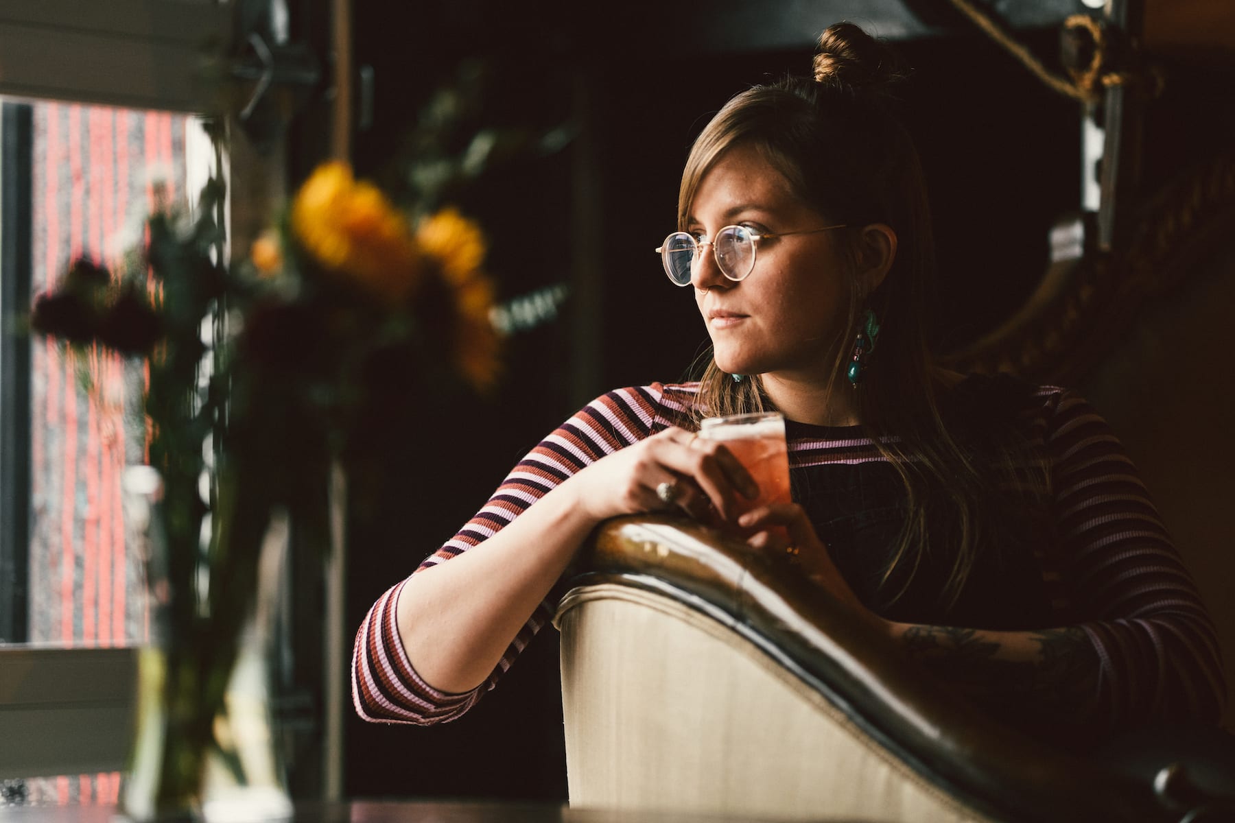 Brew Urban Cafe Woman wearing glasses in a brown striped dress shirt holding an iced drink looking off camera