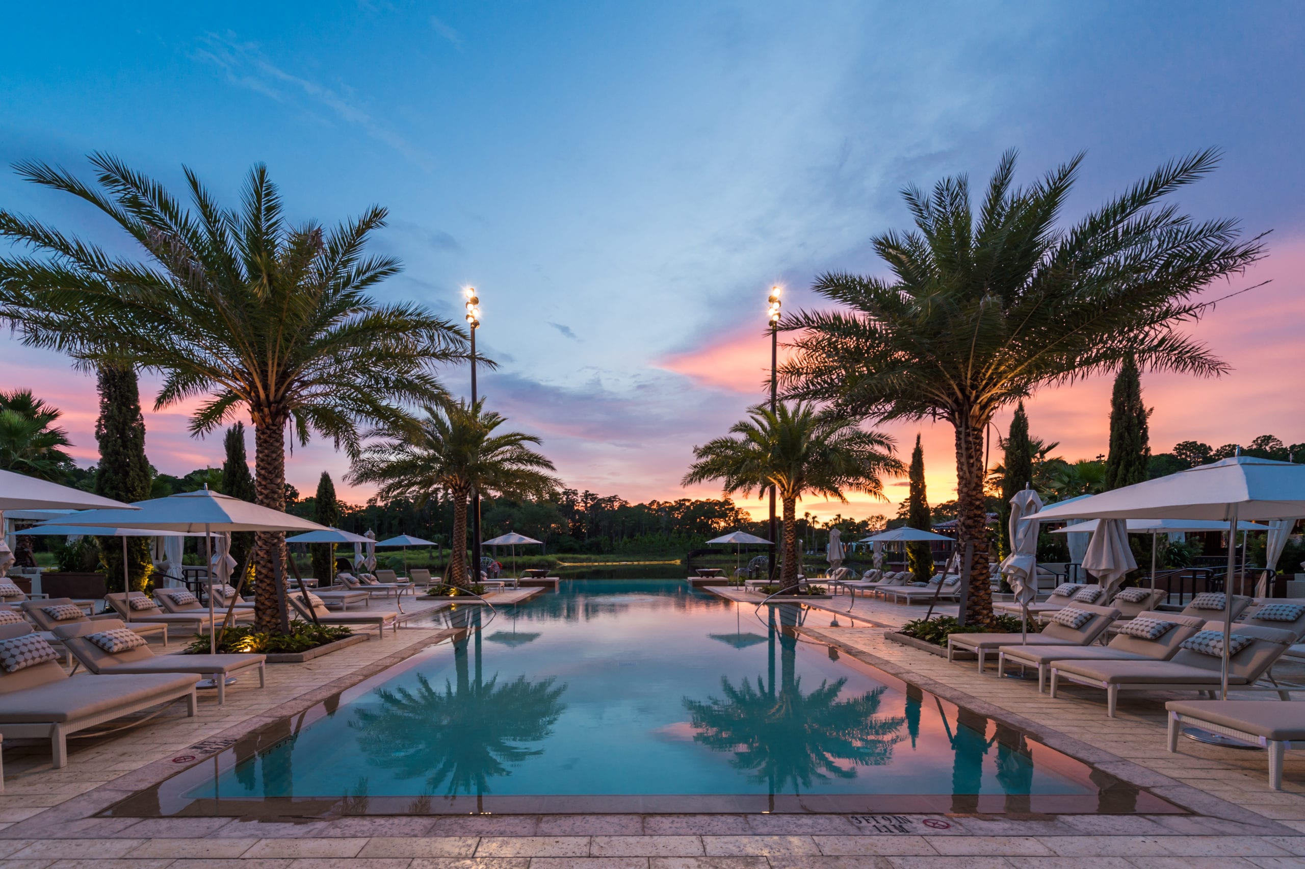 Four Seasons Pool area with lounge furniture and palm trees along with pool at dusk