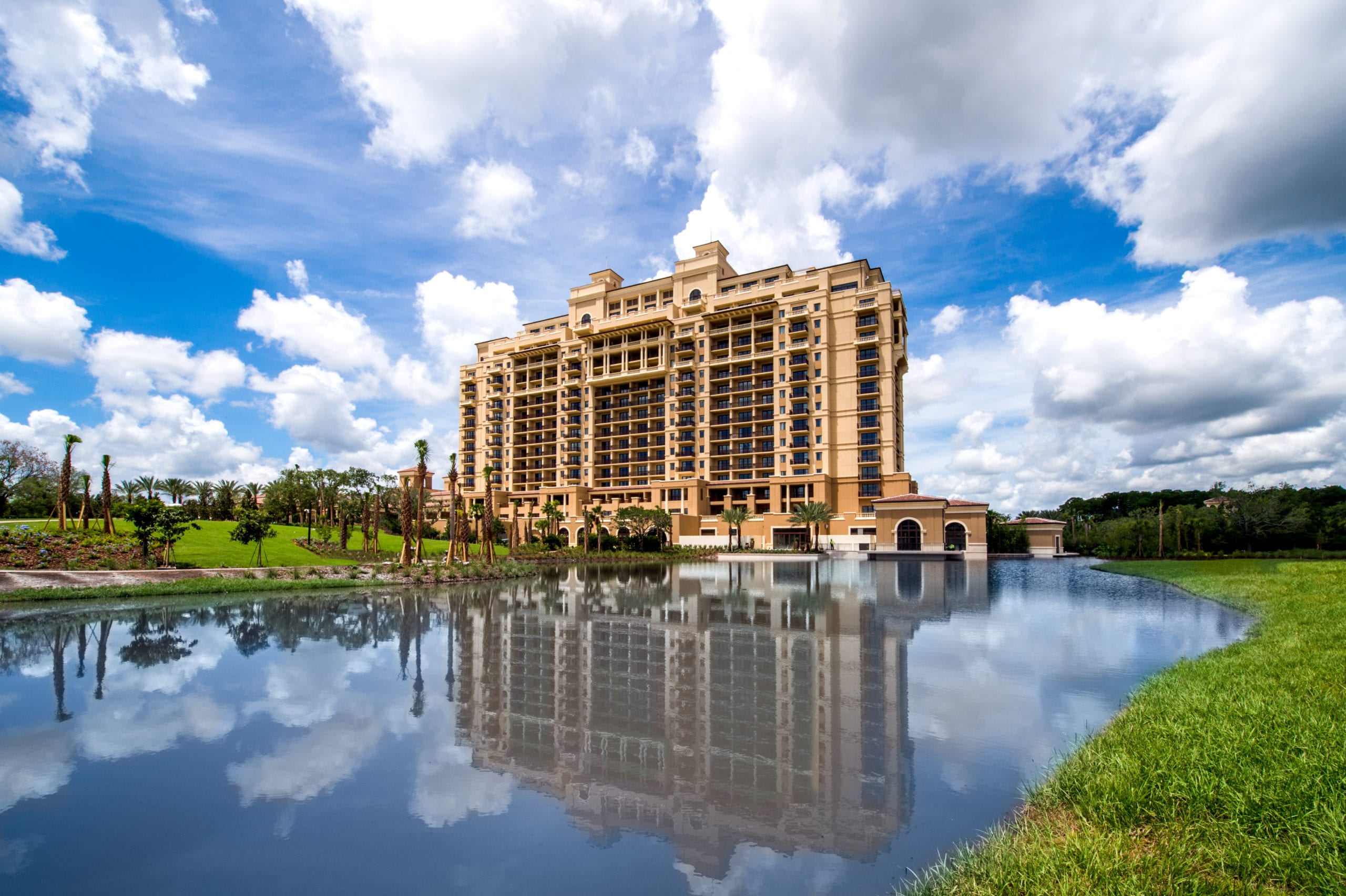 IU C&I Studios Portfolio Four Seasons Building by pond under blue cloudy skies with palm trees