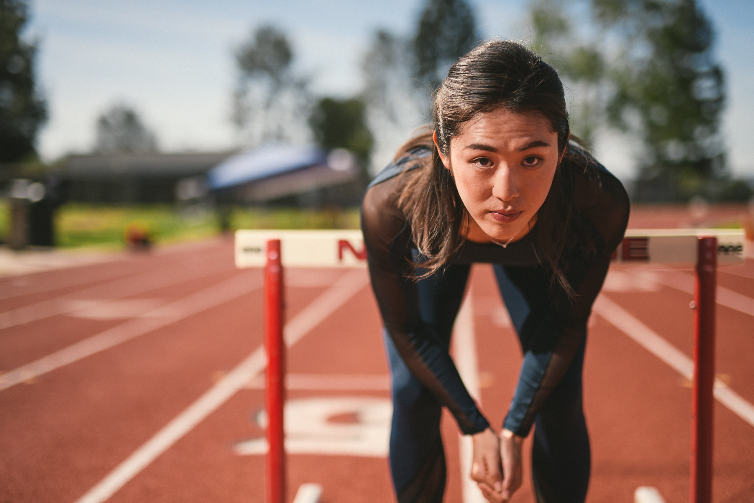 Professional Photography Services to elevate your brand C&I Studios Creative Marketing Kinetix 365 Woman posing for camera on a track field in track outfit bent over in front of a hurdle
