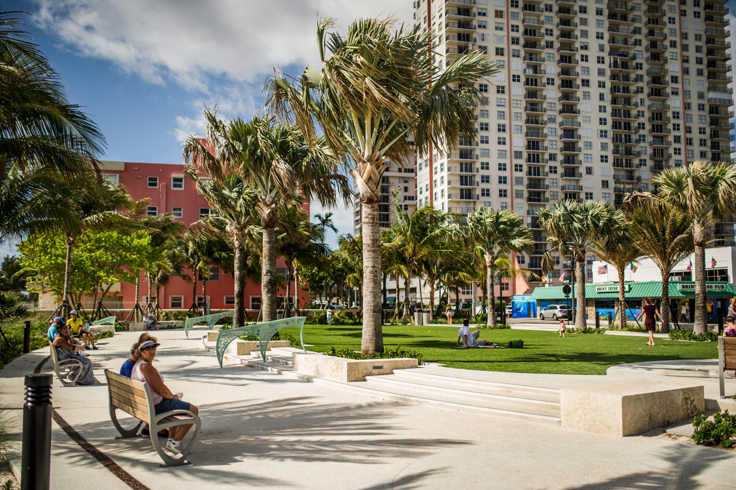 EDSA Pompano Beach Boulevard  Walkway with palm trees lining it with people sitting on benches and in a park area in the center