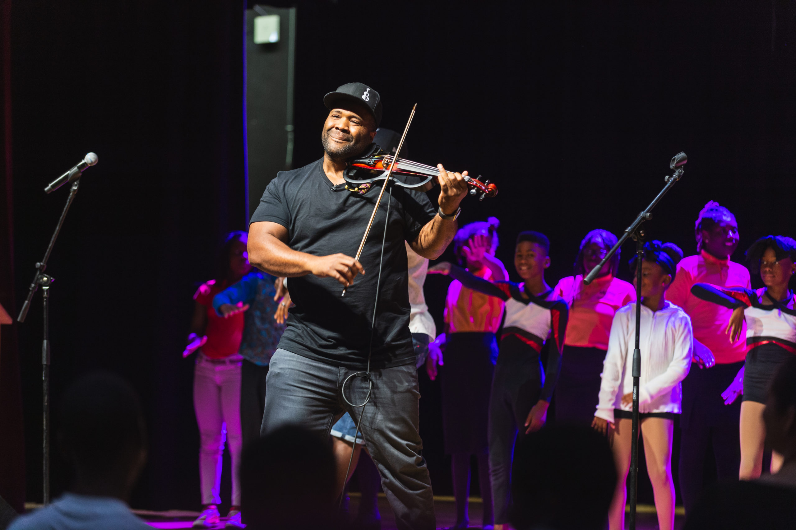 The Kennedy Center African American man wearing a black cap playing a violin with an audience of children behind him