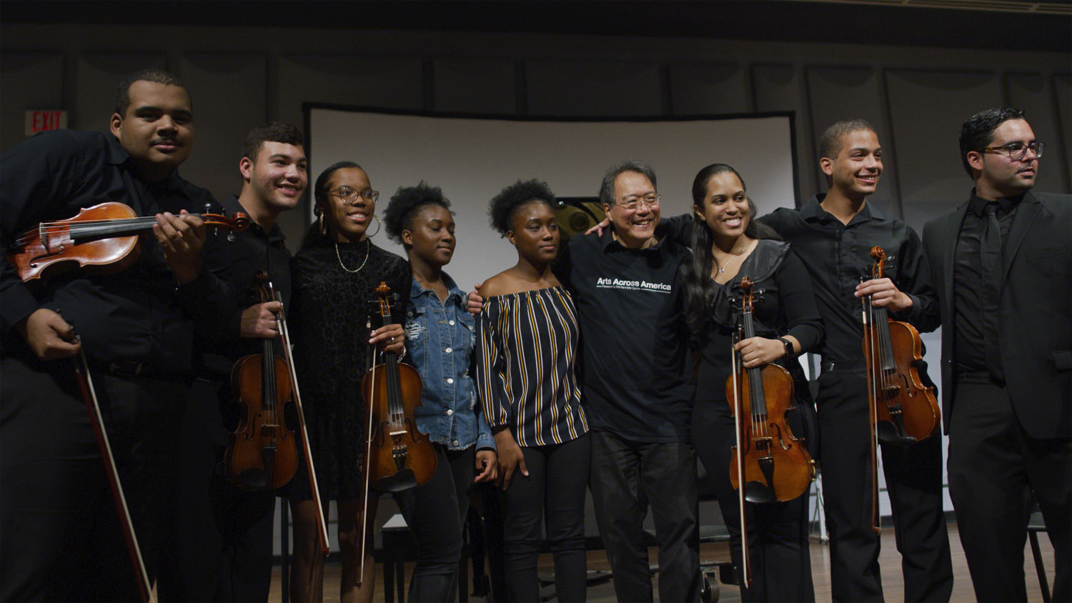 The Kennedy Center Man posing with a student band with many holding violins