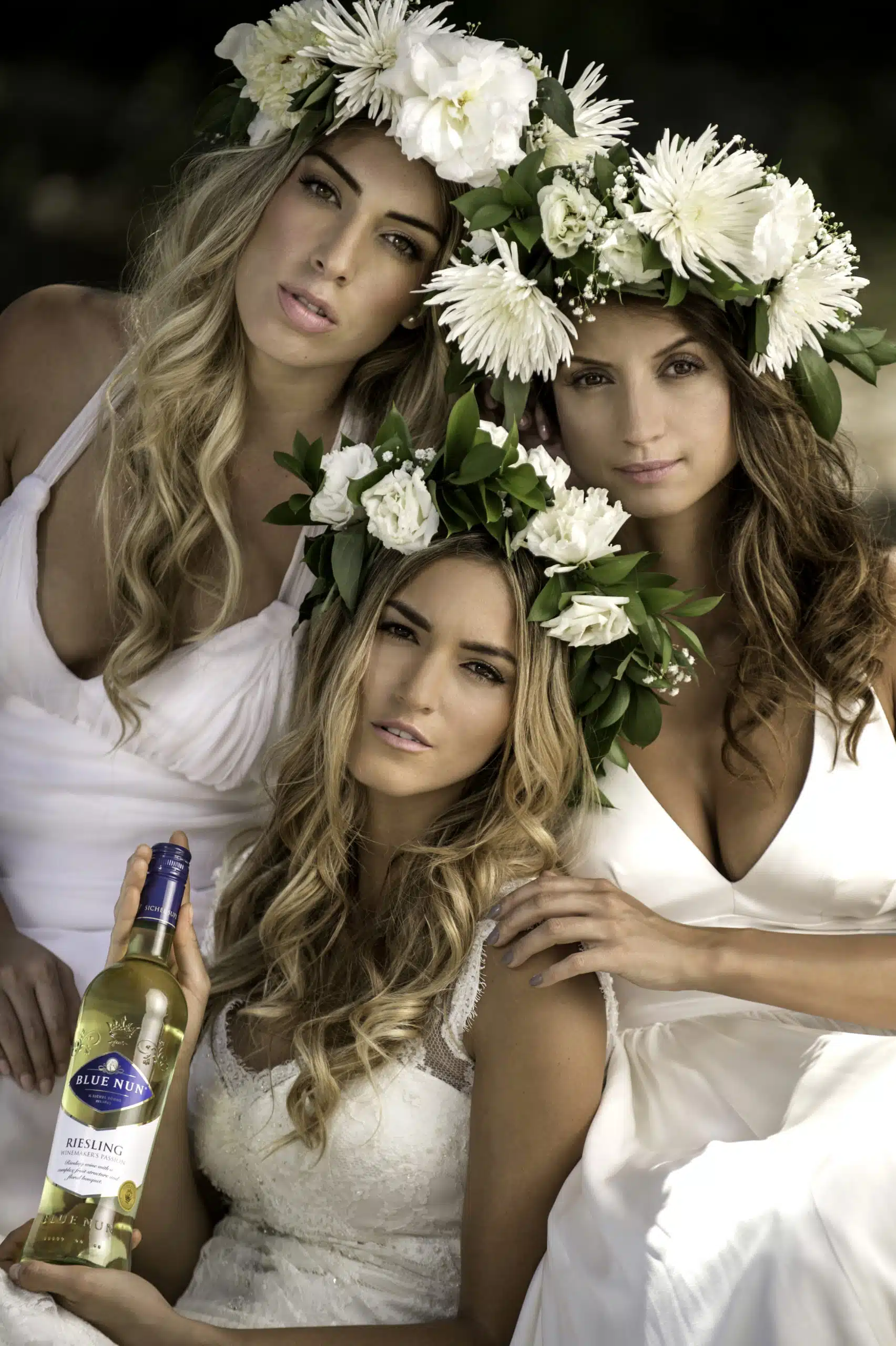 Blue Nun 8 Three women wearing flower headdresses posing for the camera wearing white dressing gowns with one holding a bottle of Riesling wine