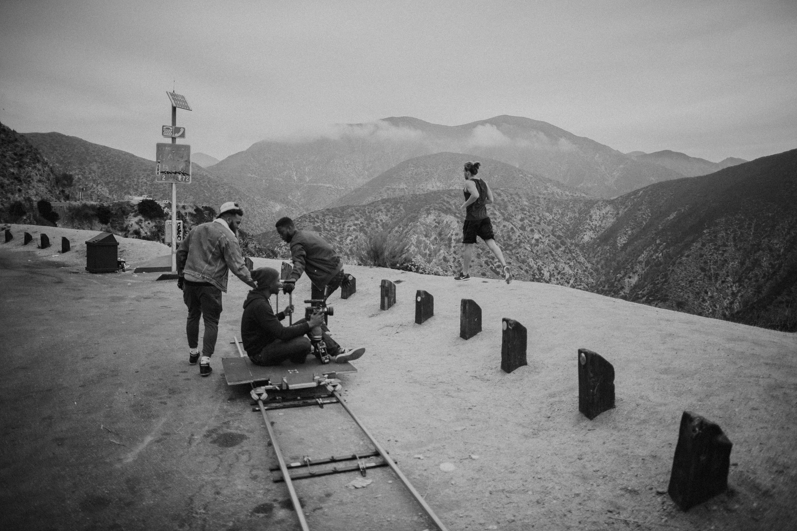 Black and white of a film crew filming a man running on a cliff