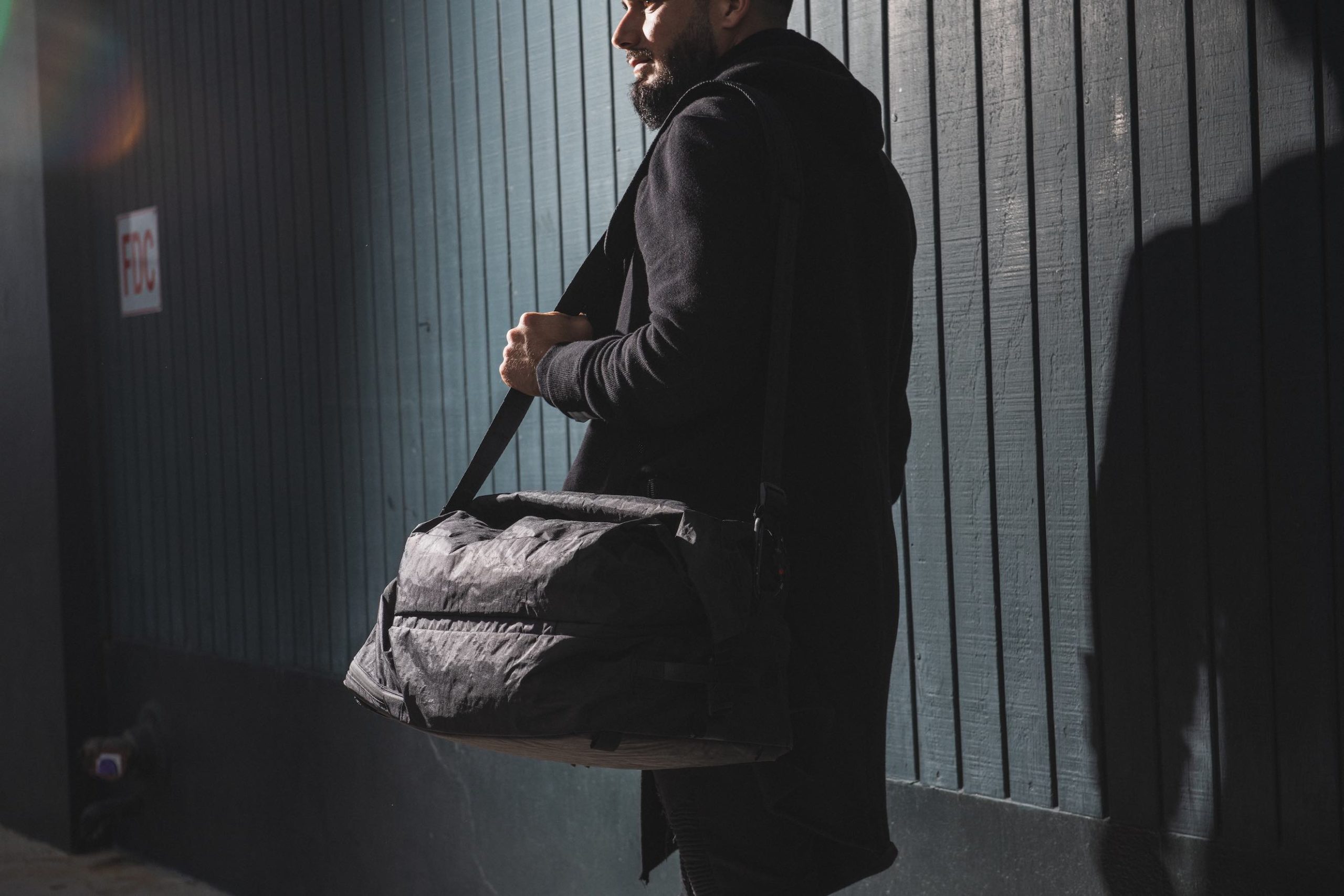 Black Mile Travel Bag Side profile of a man with a bushy beard walking with a black bag over his shoulder