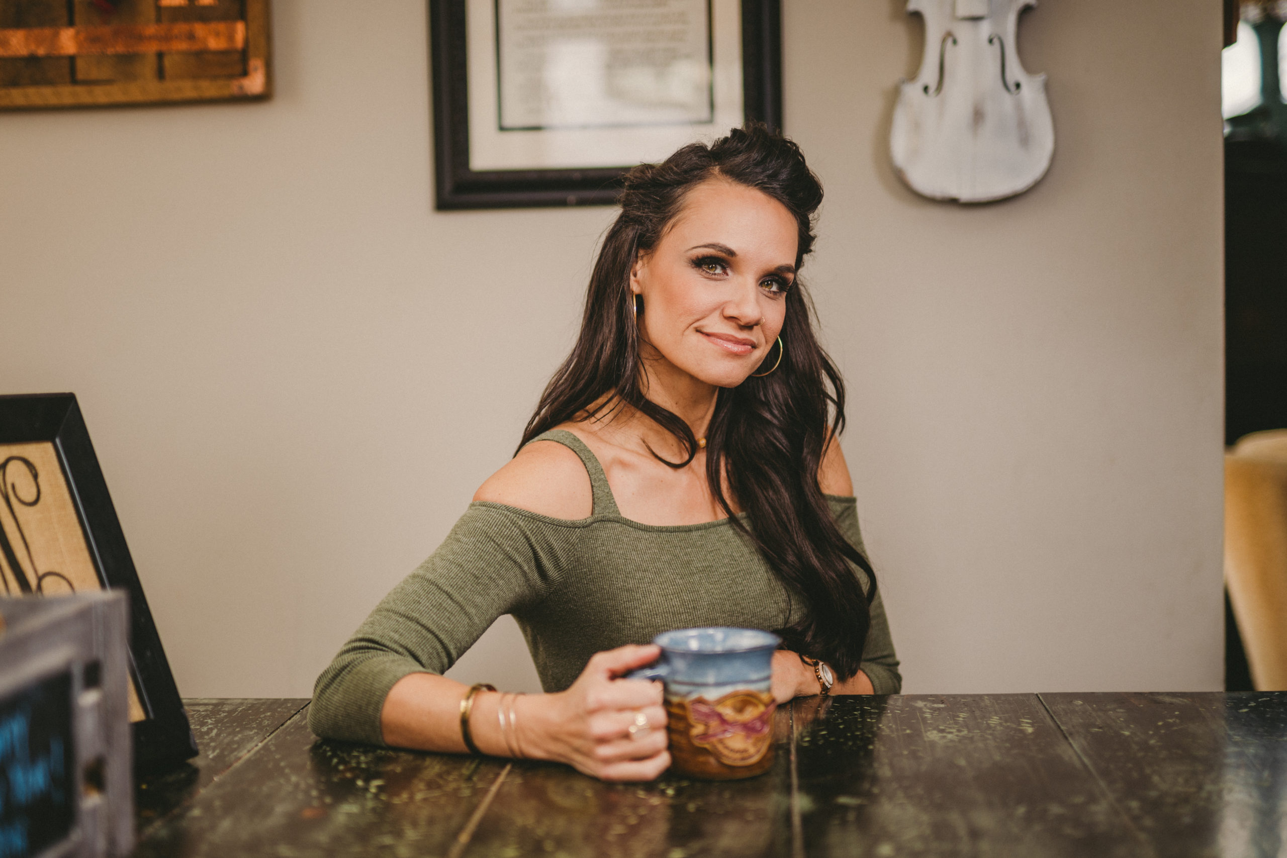JSM Woman with long brown hair posing for the camera holding a blue and brown coffee cup