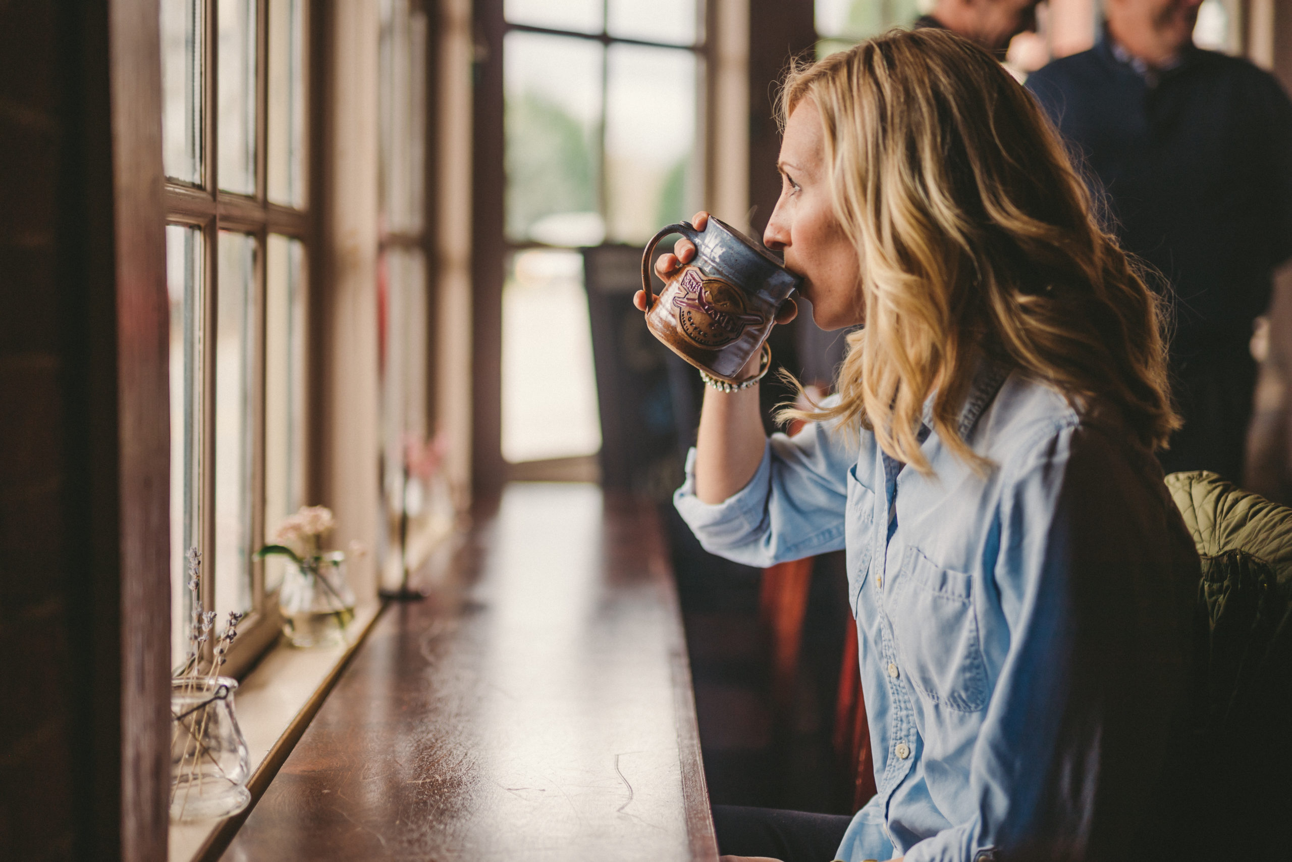 JSM Side view of woman with long blond hair drinking coffee out of a blue and brown coffee cup