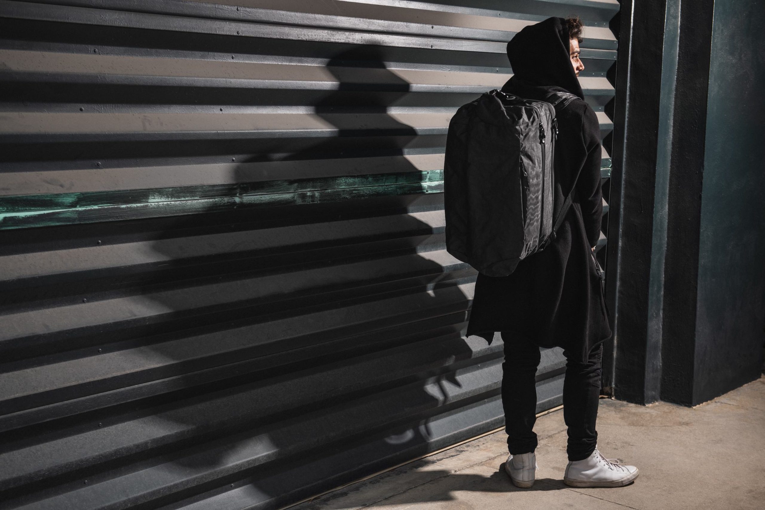 View from behind of man wearing a black backpack and a black coat standing by a metal garage door