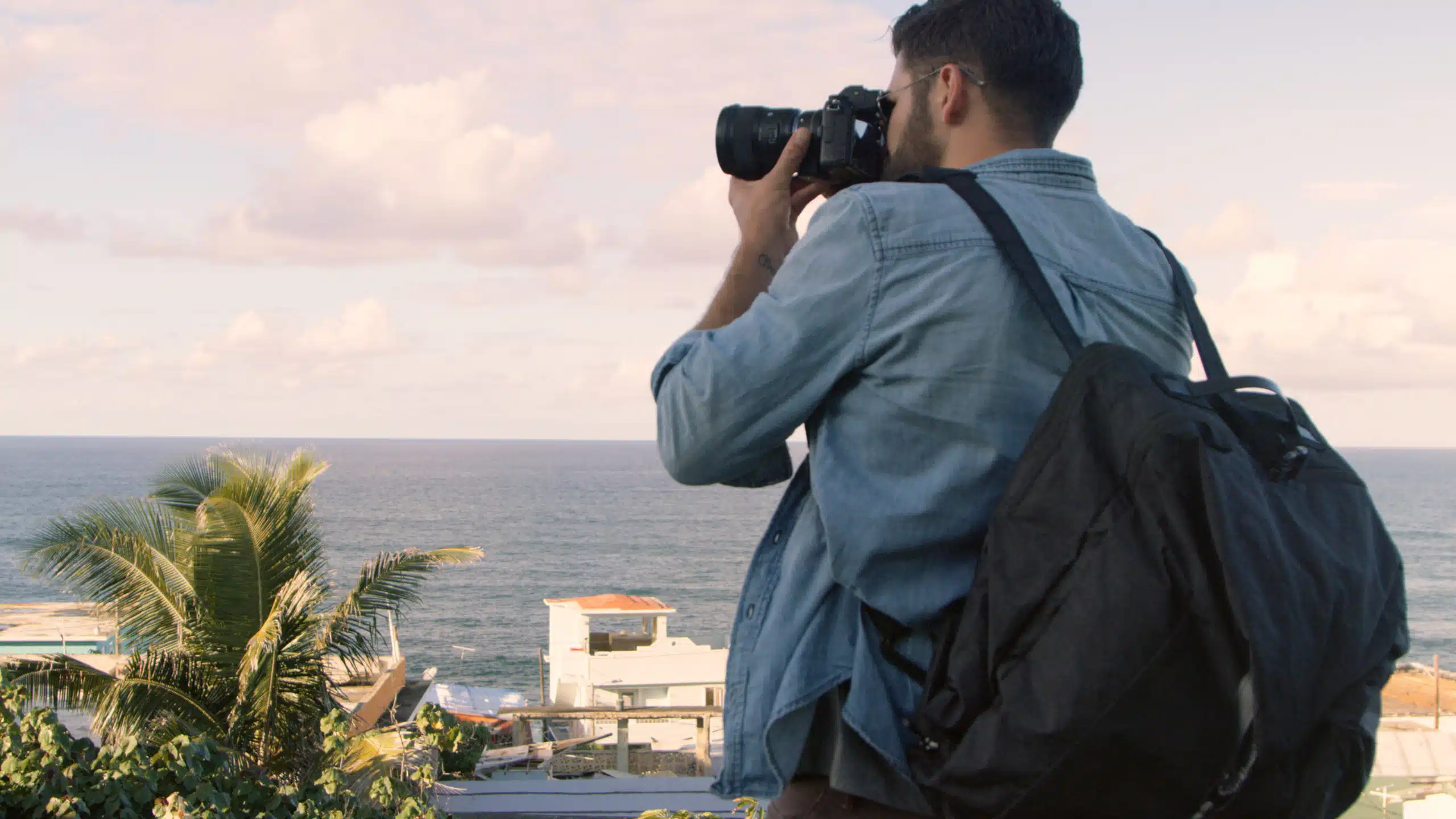 Closeup view from behind of a man wearing a black backpack taking a picture
