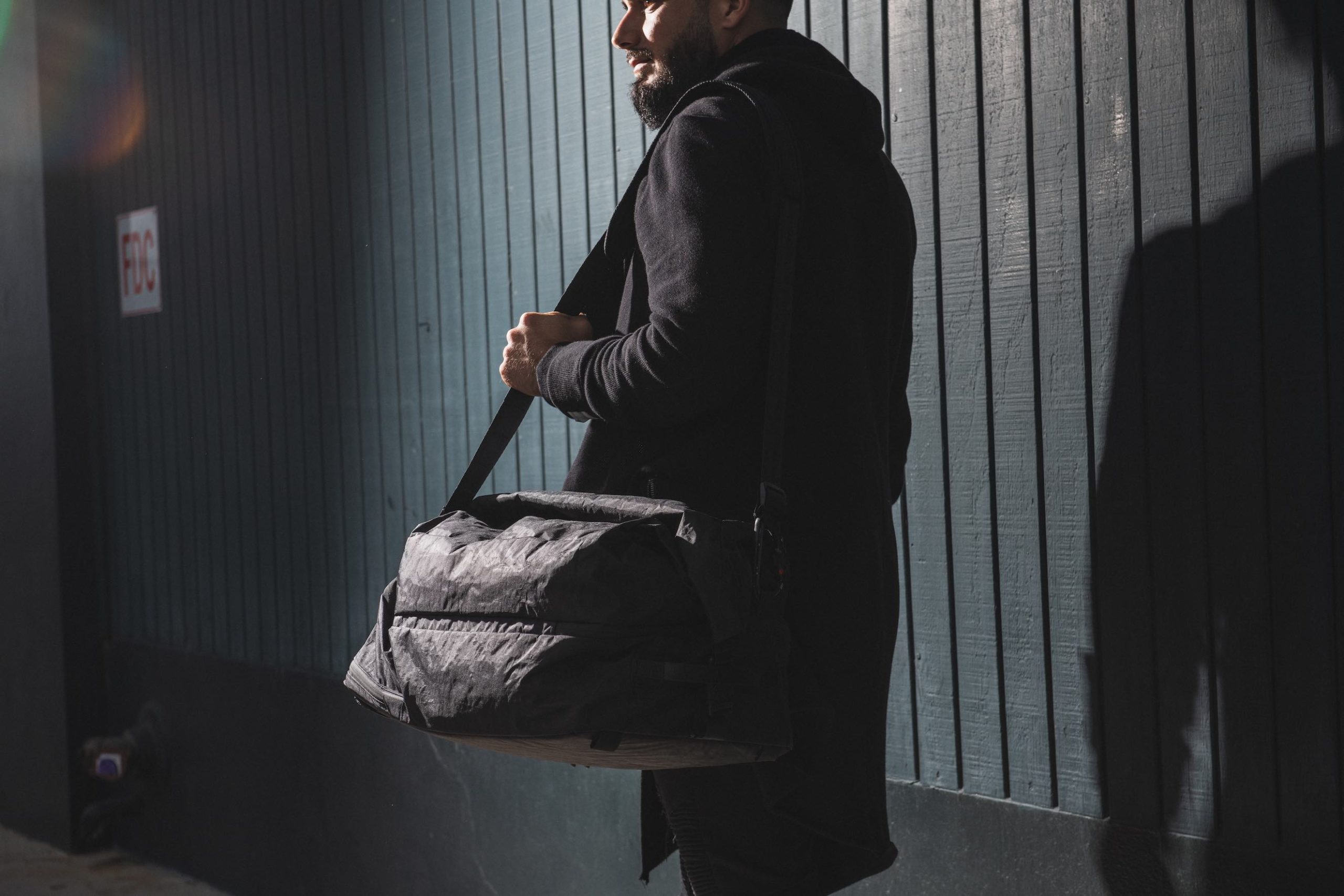 Side profile of a man with a bushy beard walking with a black bag over his shoulder