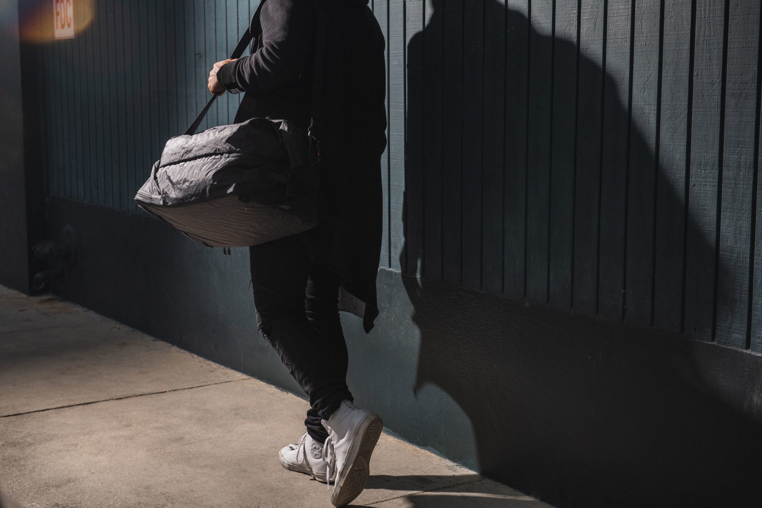 View from behind of a man walking carrying a black bag on his shoulder