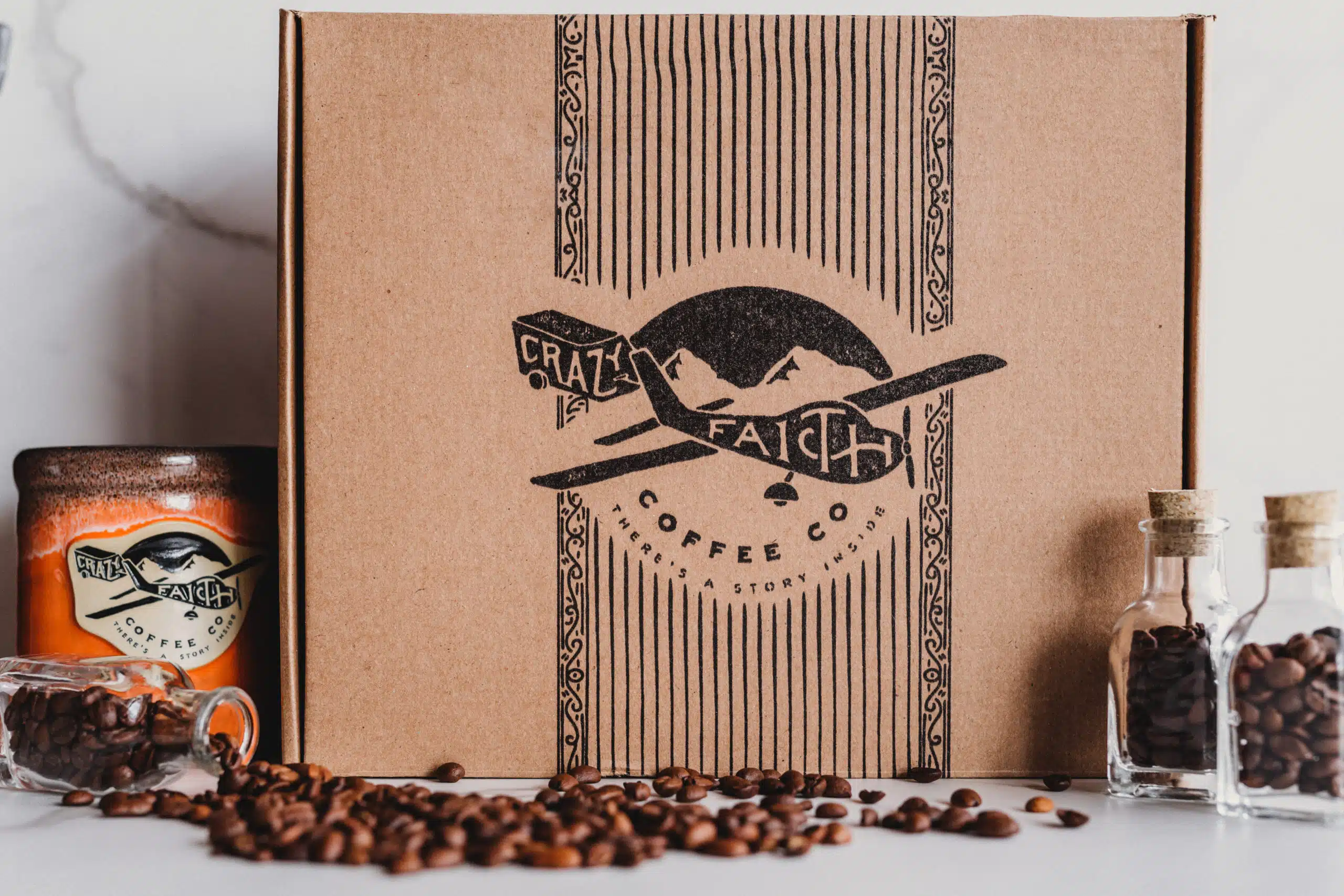 Crazy Faith Coffee 23 Closeup of the Crazy Faith box along with brown and orange coffee cup, coffee beans and three vials of beans