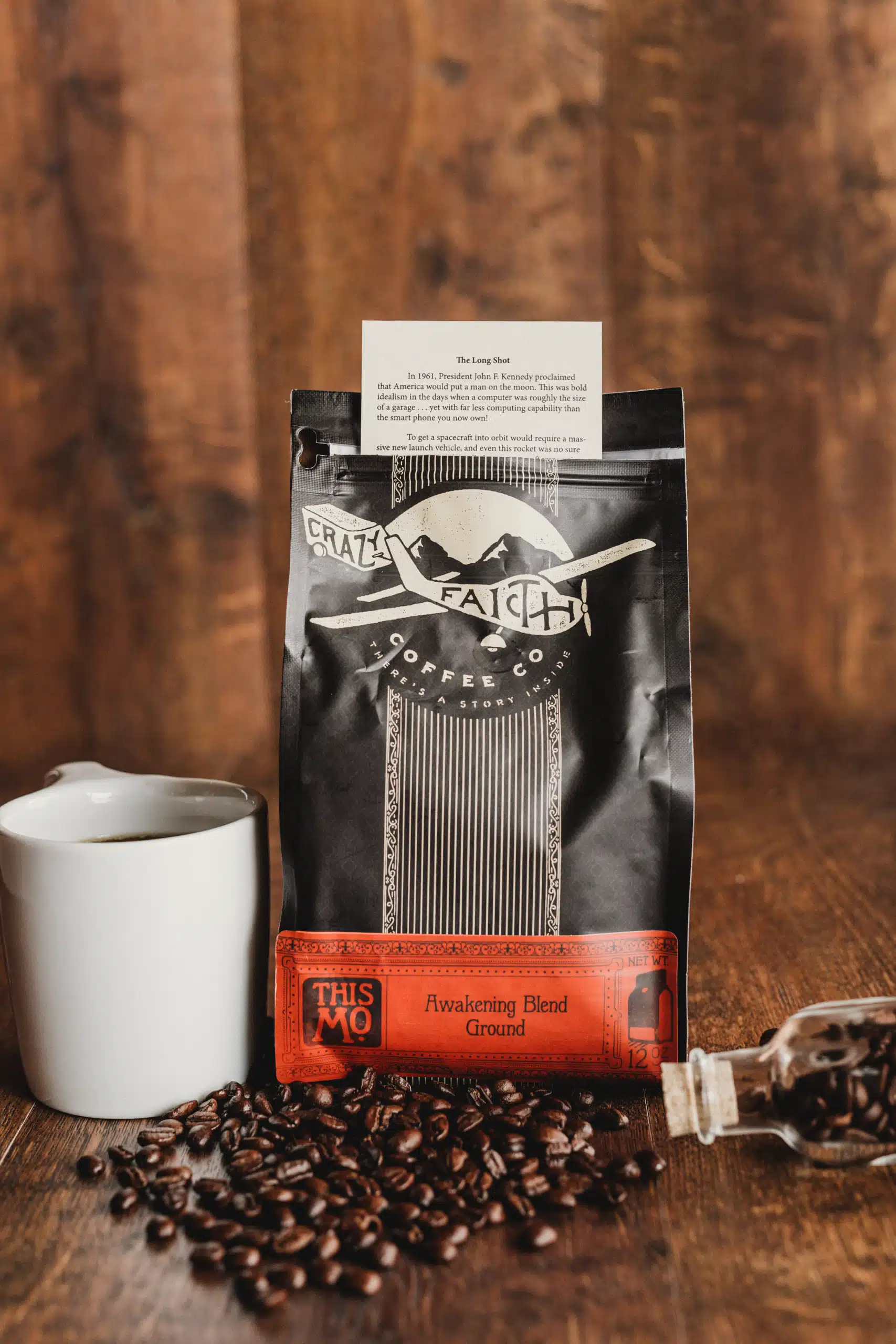 Crazy Faith Coffee 32 Package of Awakening Blend Ground coffee beans along vial and coffee beans on the wooden table along with white coffee cup with coffee