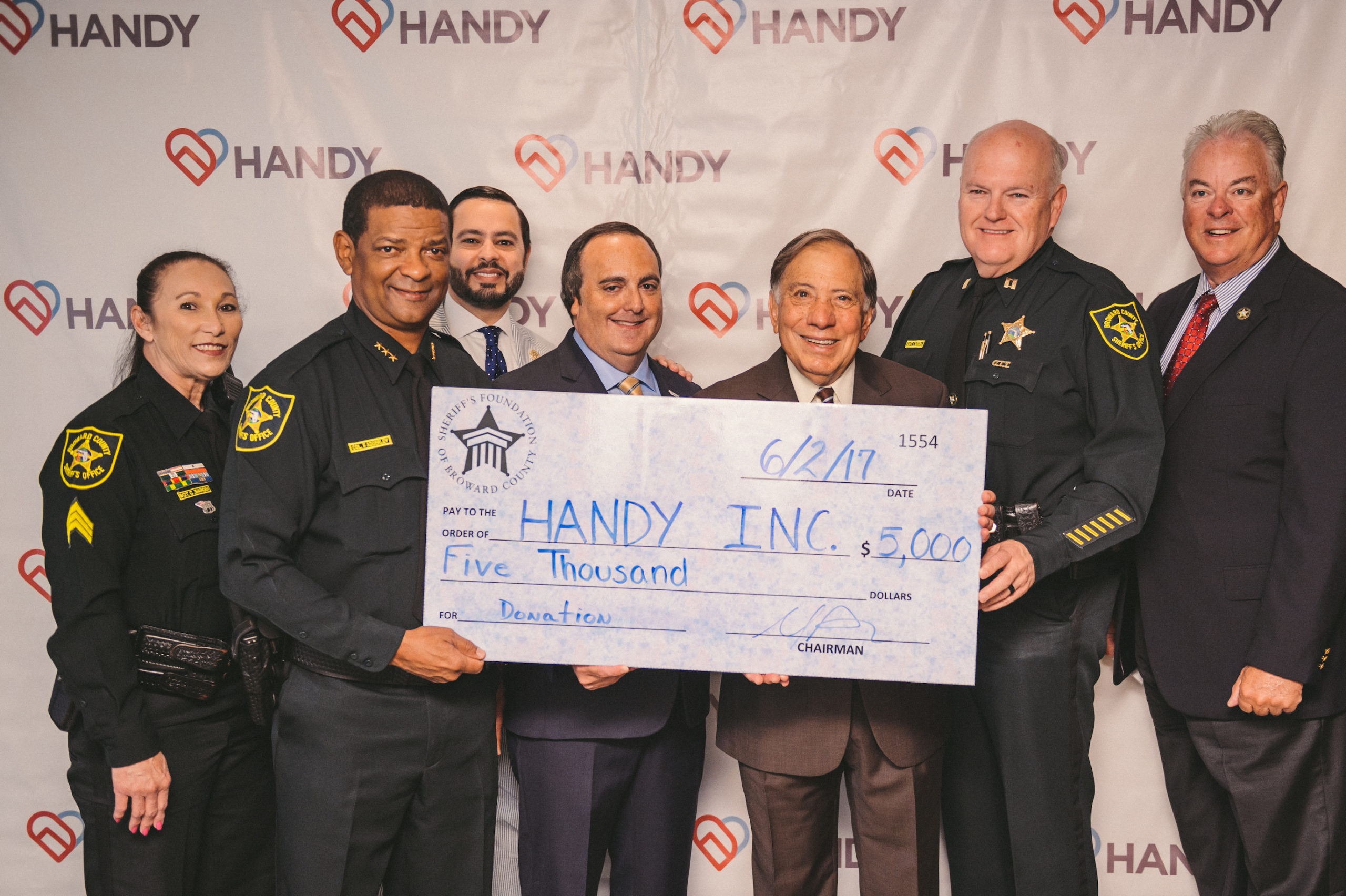 Handy Inc Donation check being held by two people surrounded by police officers