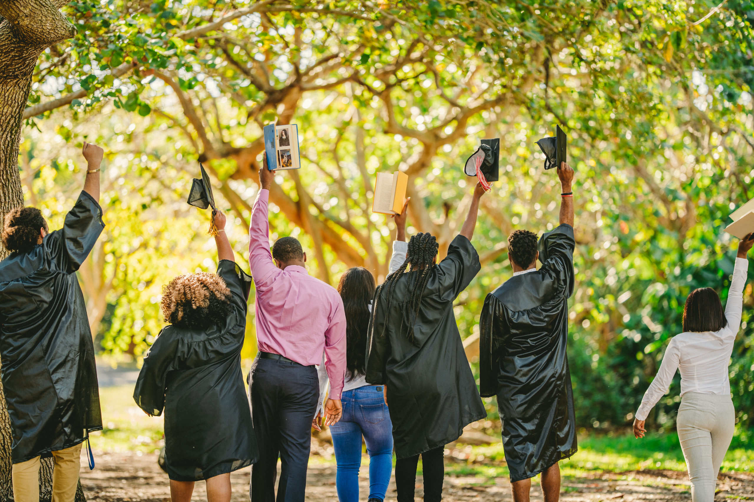 Handy Closeup from behind of group of two male and two female graduates walking with two women holding books and one male wearing a pink shirt