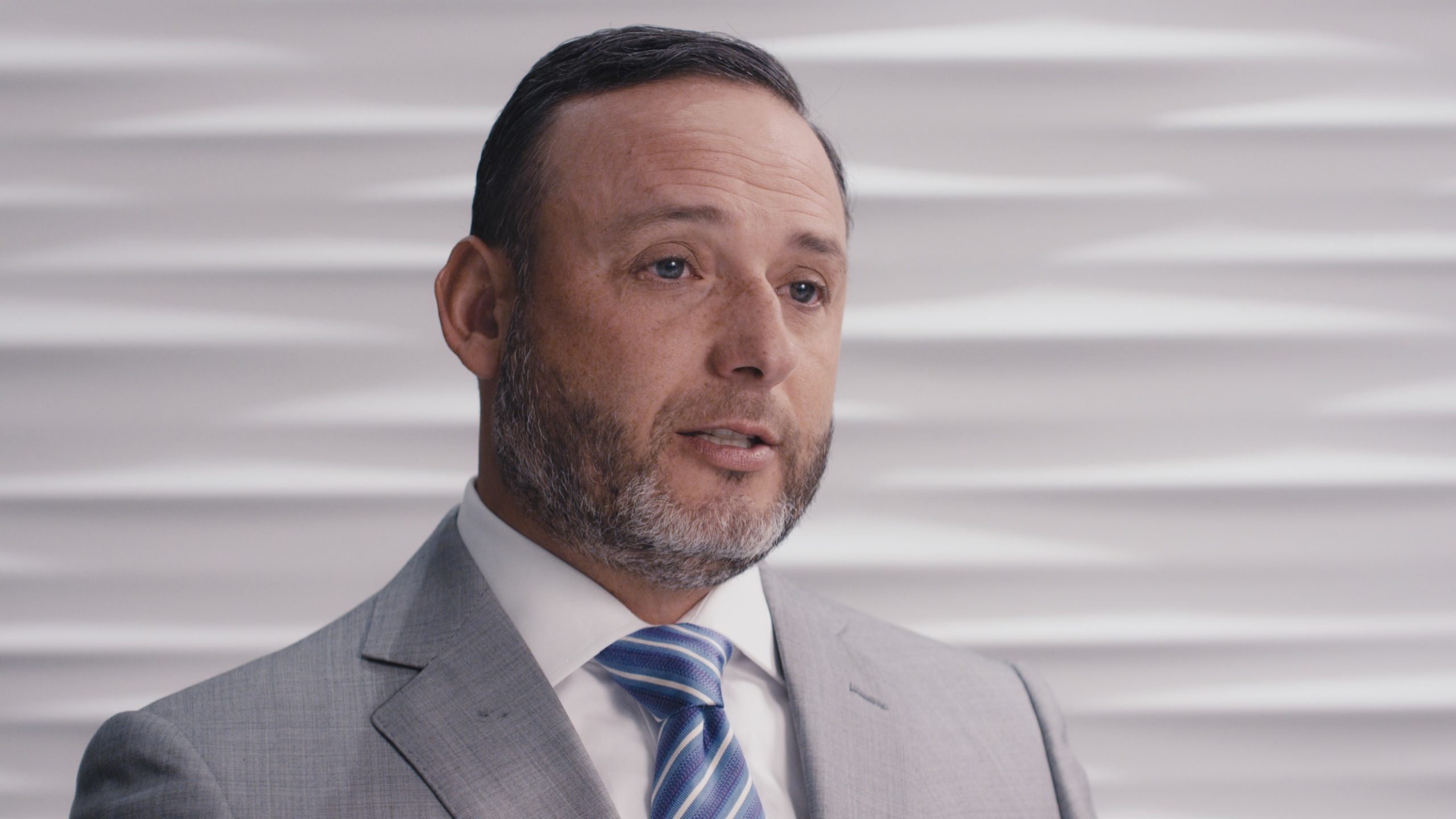 Hightower Financial Advisors Headshot of a man with a salt and paper beard wearing a gray suit with white shirt and blue tie