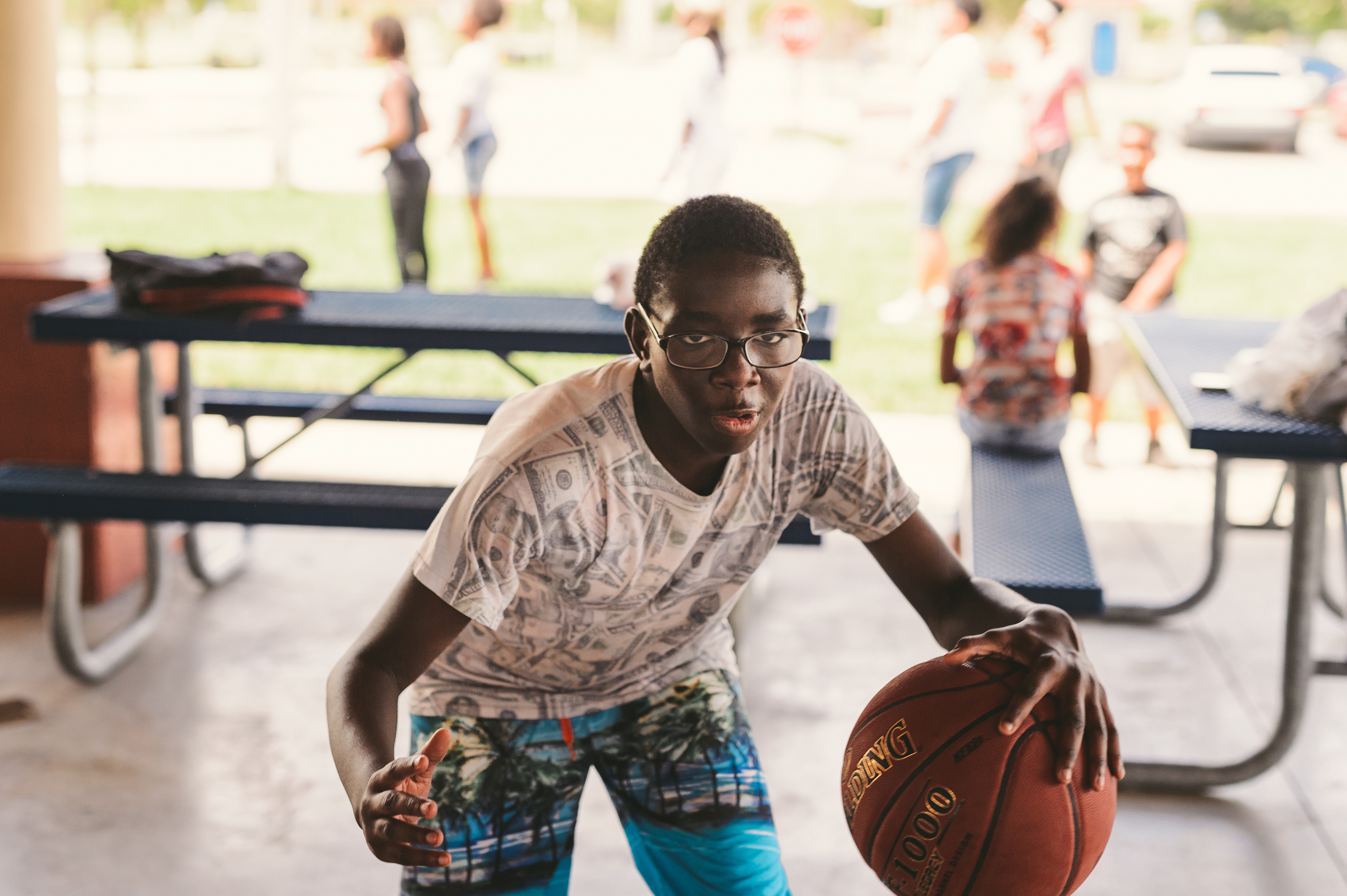 KES African American young adult wearing bermuda shorts and t shirt with money graphics on it posing for the camera with a basketball in a pavilion
