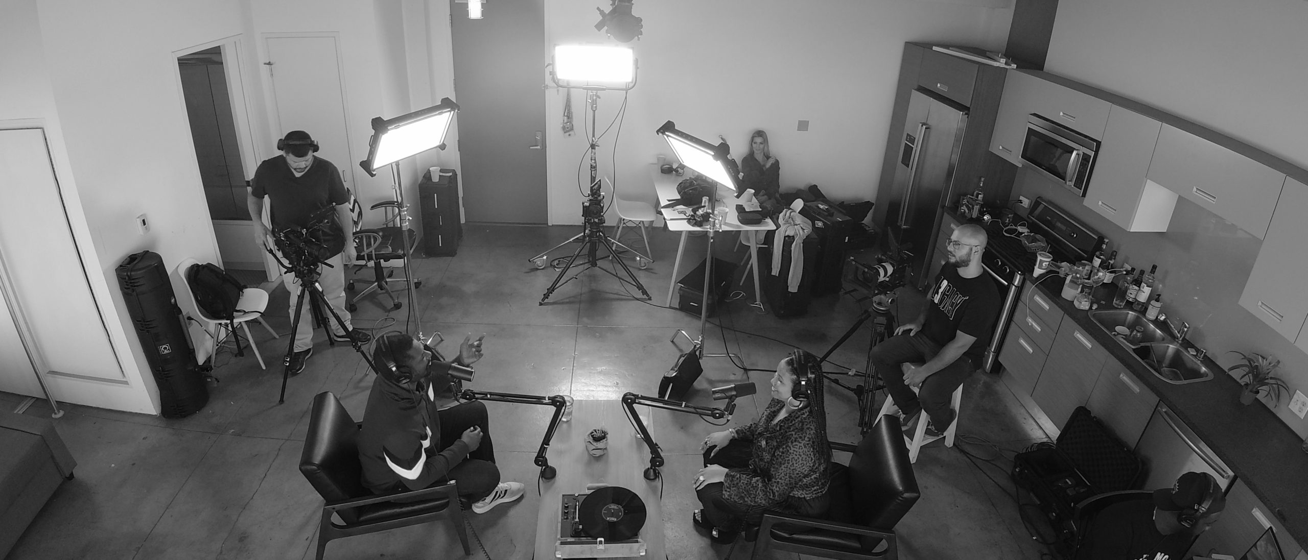 Black and white still of a radio show in progress with five people in the room
