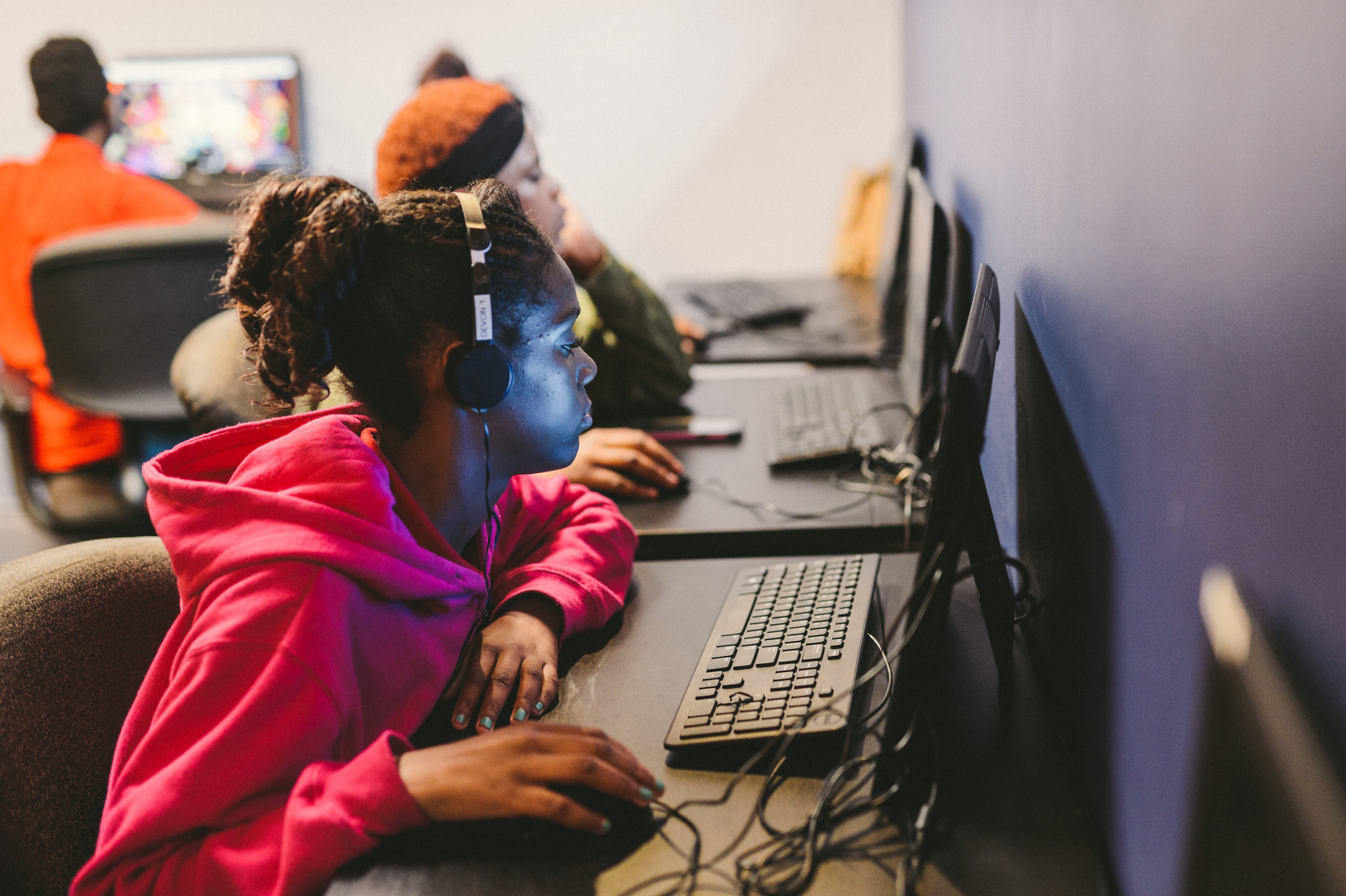 Side profile of African American young woman using a computer with other people in background also using computers