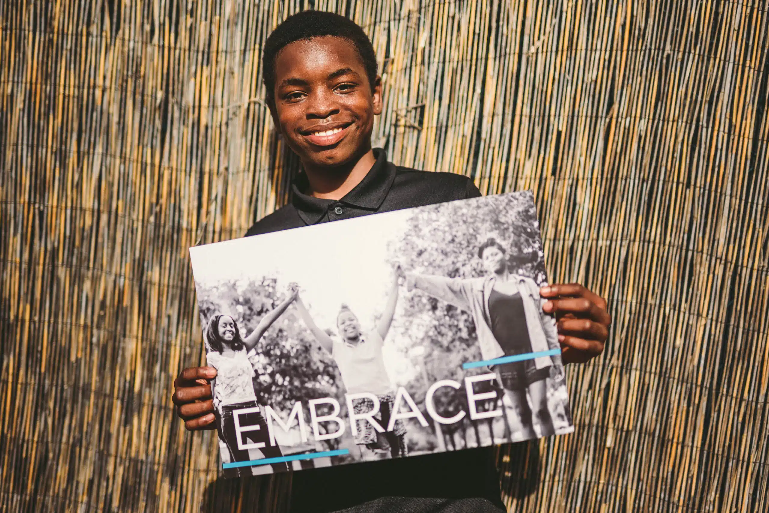 Handy 32 African American holding a black and white poster that shows three people with the word Embrace