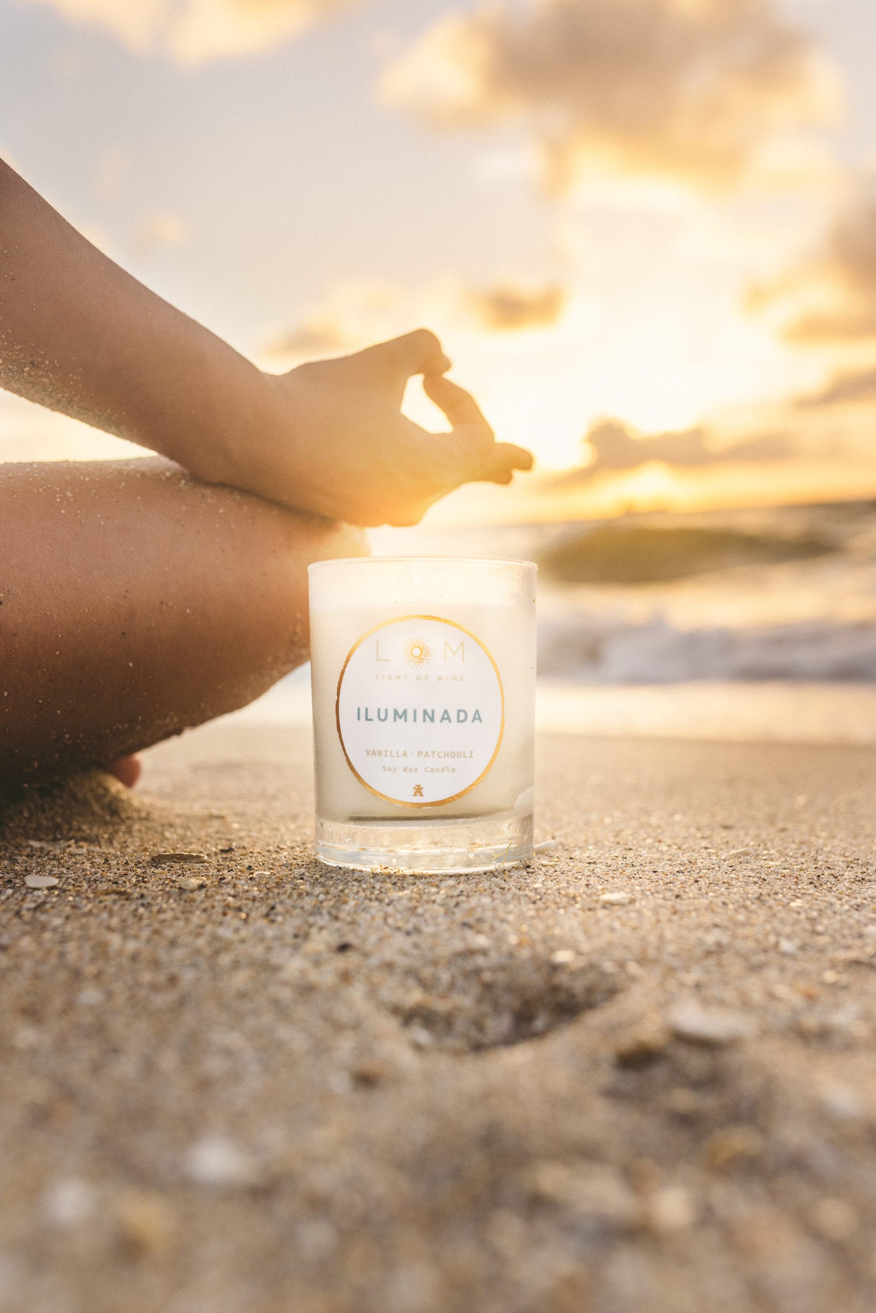 Sand covered person doing Yoga ooommm next to Light of Mine soy wax candle on a beach with bright sunshine.