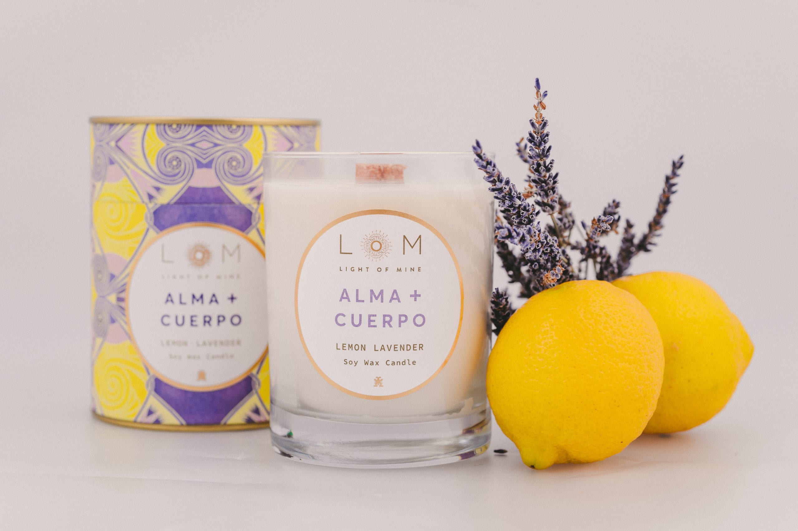 Two Light of Mine Alma and Cuerpo brand with Lemon Lavender soy wax scented candles next to sprig of lavender and two lemons