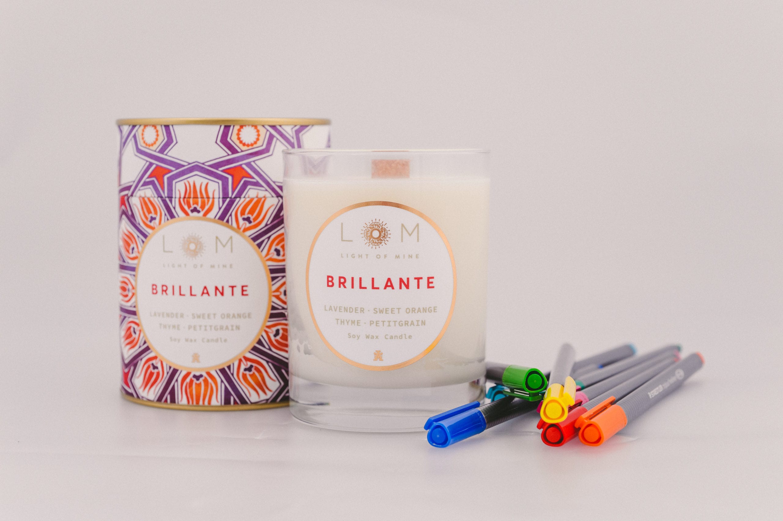Two Light of Mine Brillante brand with Lavender, Sweet Orange, Thyme and Petitgrain soy wax scented candles with different colored markers nearby