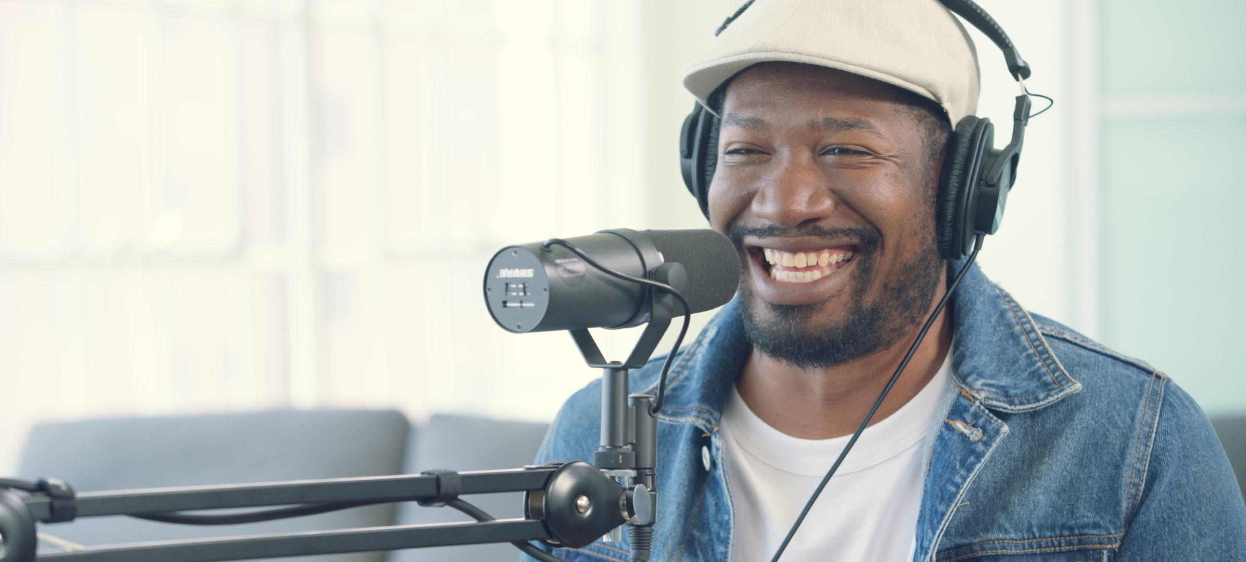 Uncreative Radio in L.A. Episode 109 Pavvlo Zengo African American man with a beard wearing headphones and a blue jean jacket smiling and talking in a microphone
