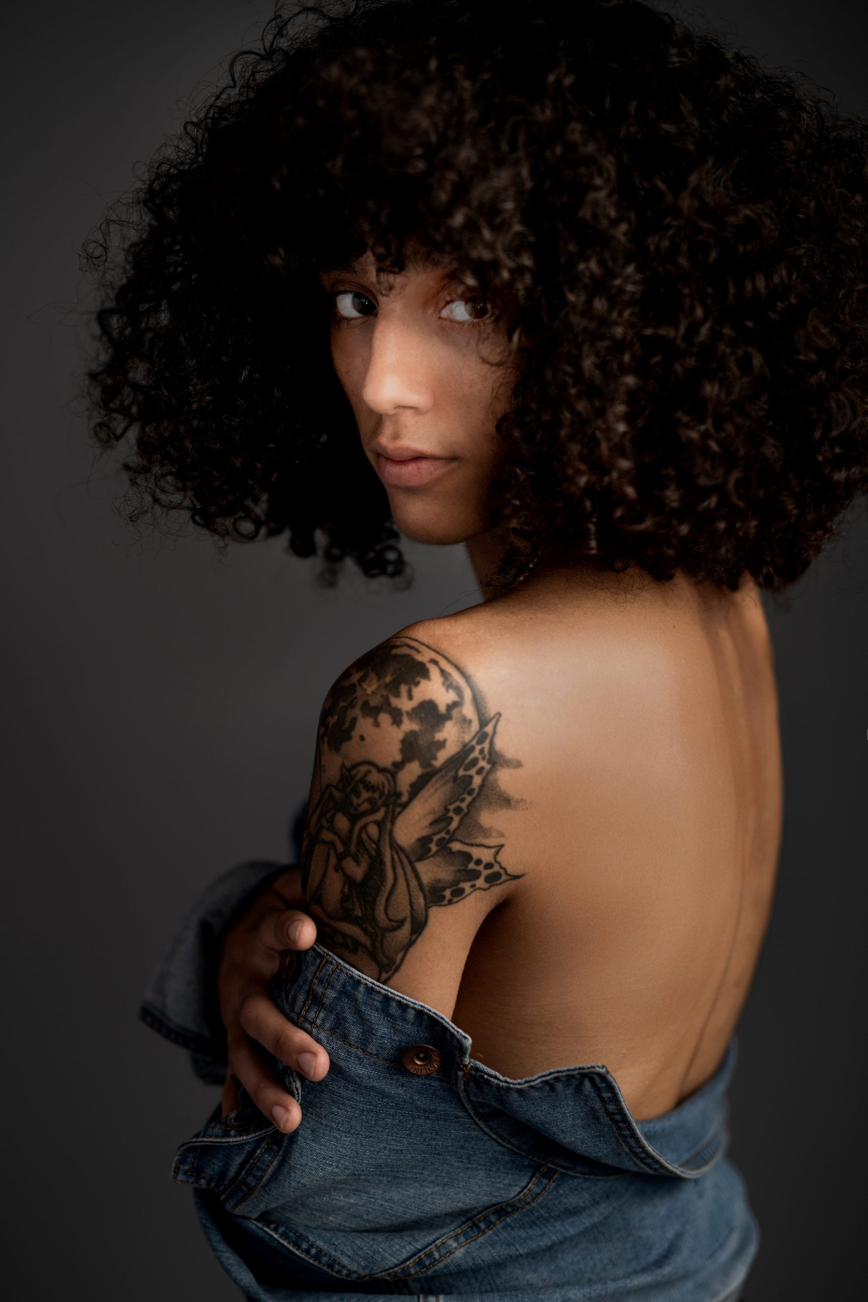 IU C&I Studios Post South Florida Model Jasmine with black poofy hair looking over her tattooed shoulder into the camera