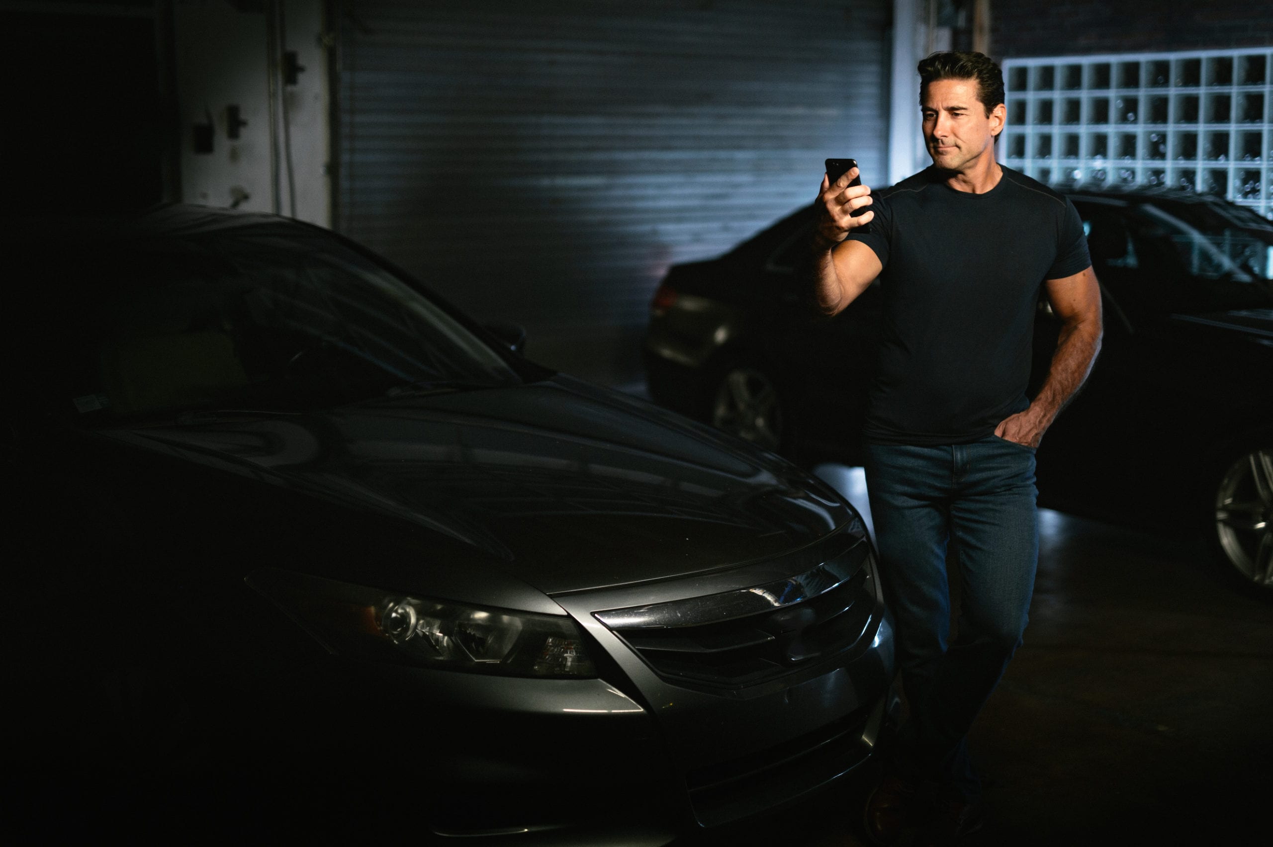 Car Offer Young muscled man holding a cell phone standing between two black cars