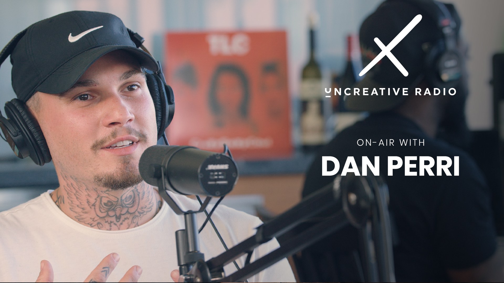 Uncreative Radio on air with Dan Perri with owl tattoo on neck wearing black cap and headphones by microphone