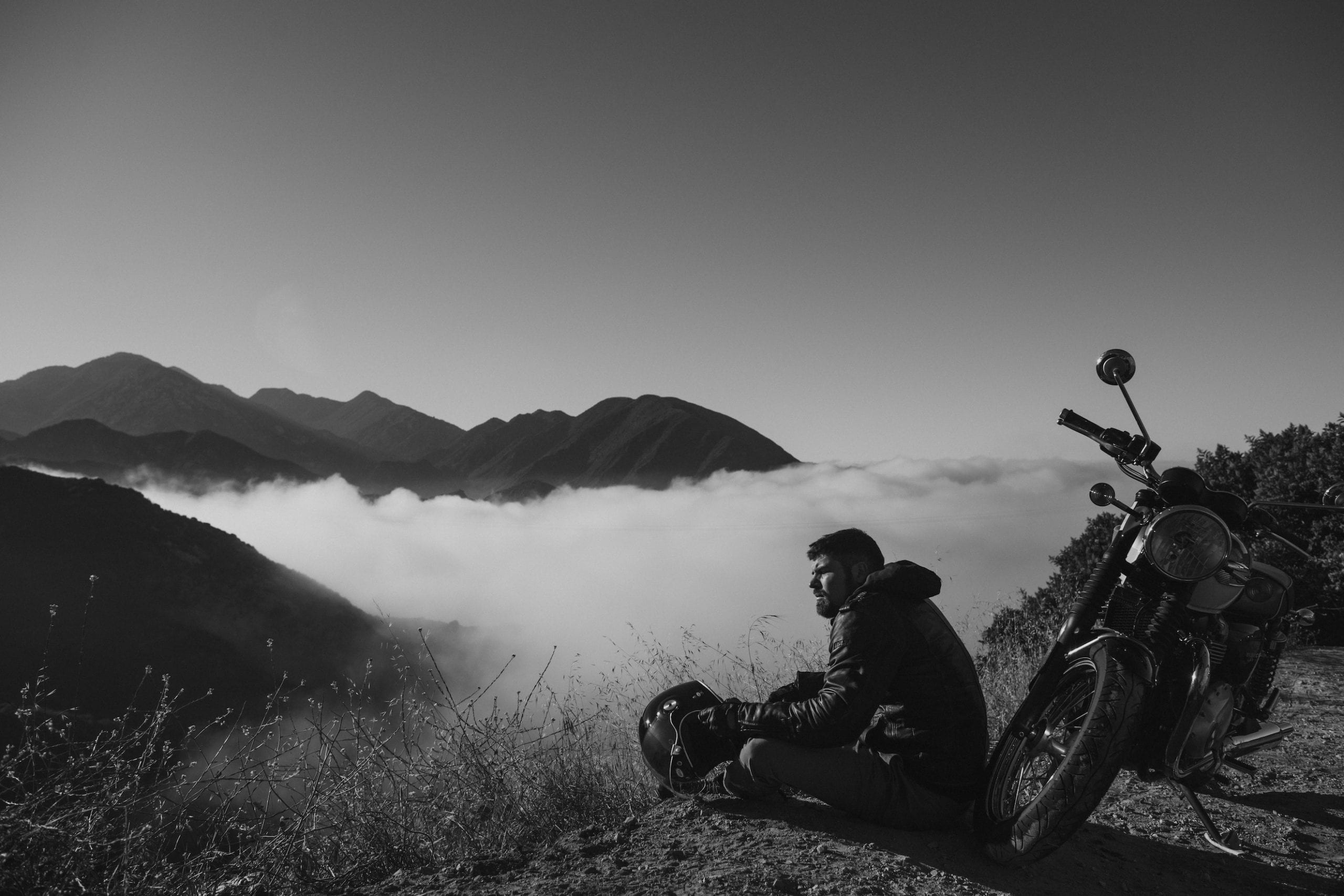 IU CI Studios Portfolio Triumph Euro Bike Shoot Black and white photo of a motorcycle rider resting above the clouds overlooking a mountain range.