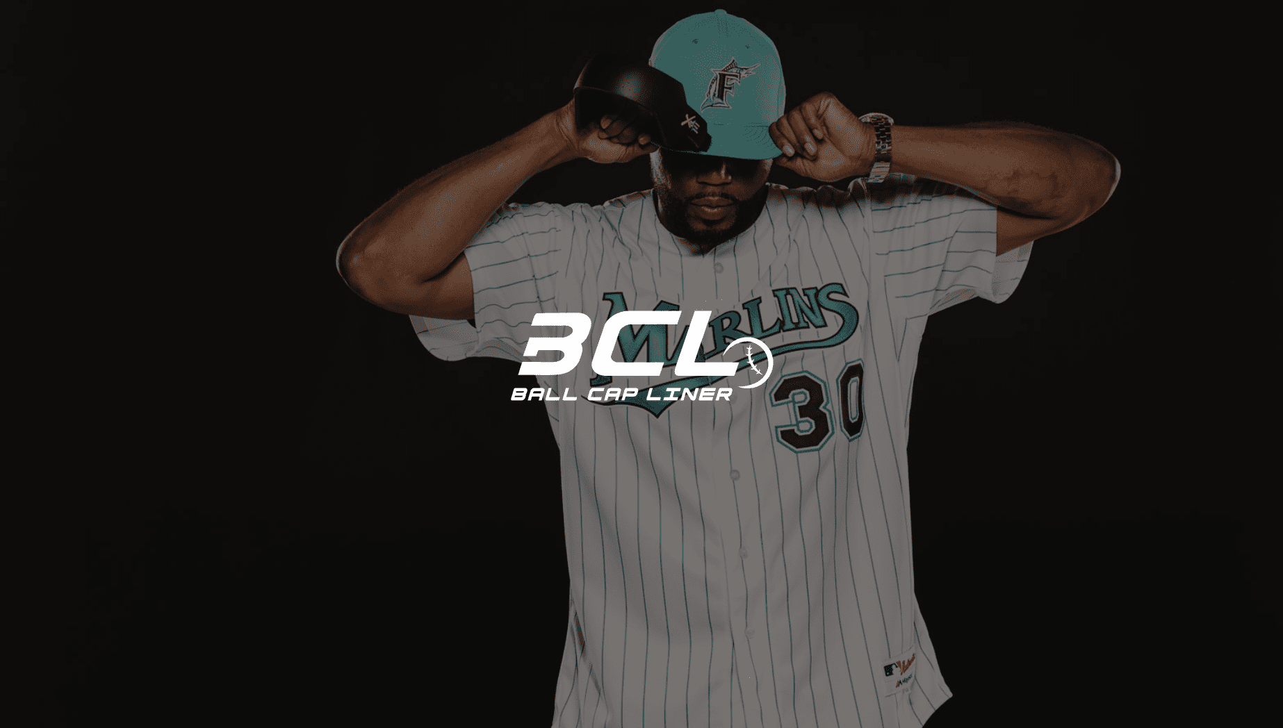 White BCL Ball Cap Liner logo against an African American man wearing a Marlins jersey and cap posing for the camera looking down adjusting his cap