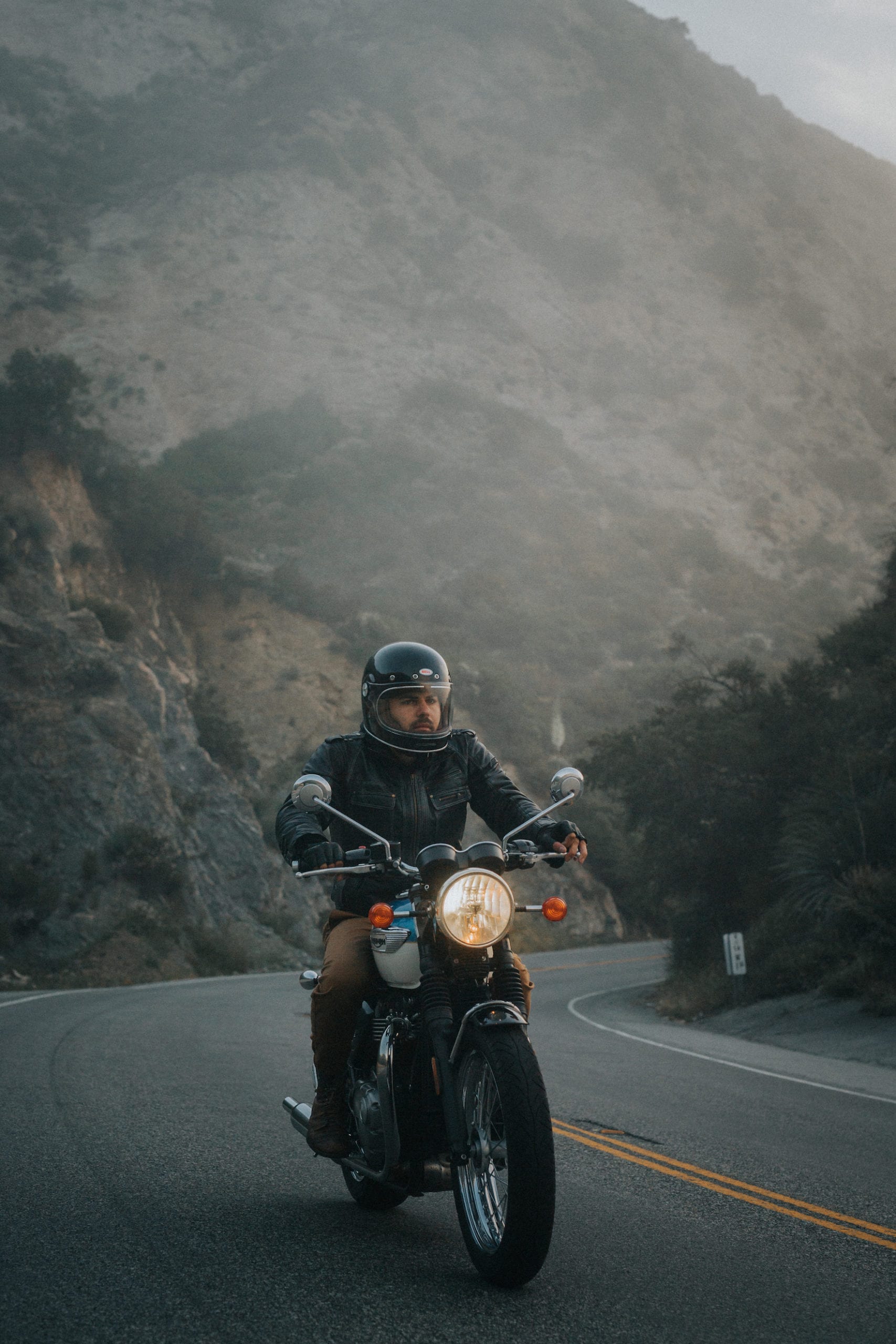 Triumph Motorcycles Euro Bike Photography Motorcycle rider wearing a helmet and motorcycle gear riding up the mountain on a hazy morning.