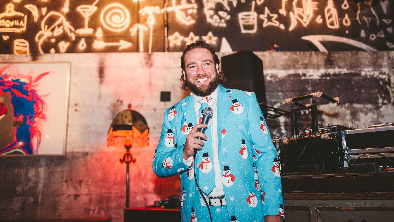 Van Horn Man wearing a light blue jacket and tie with graphic snowmen on it smiling and holding a microphone