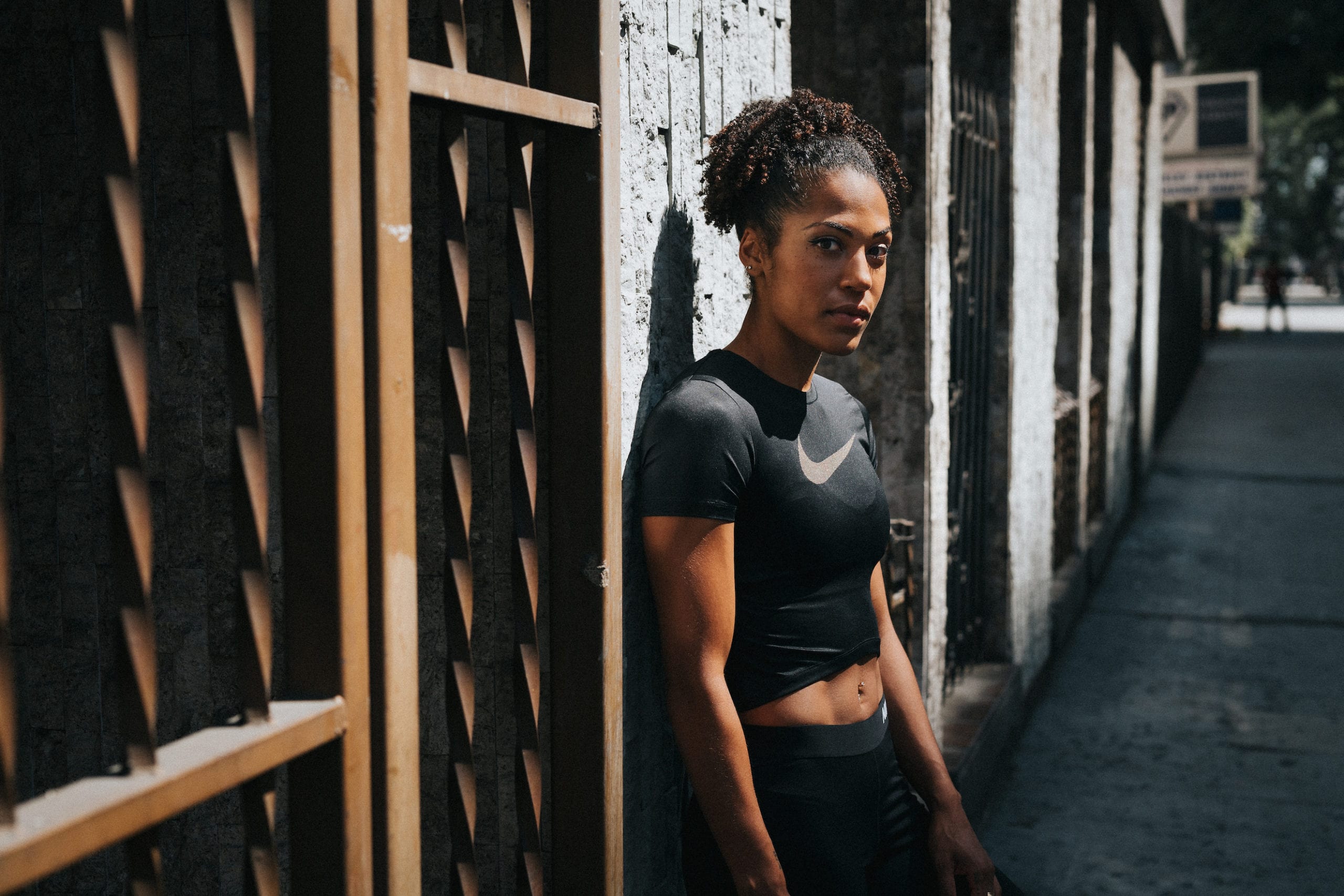 Karelle Edwards side profile leaning against gray building next to a gold colored gate