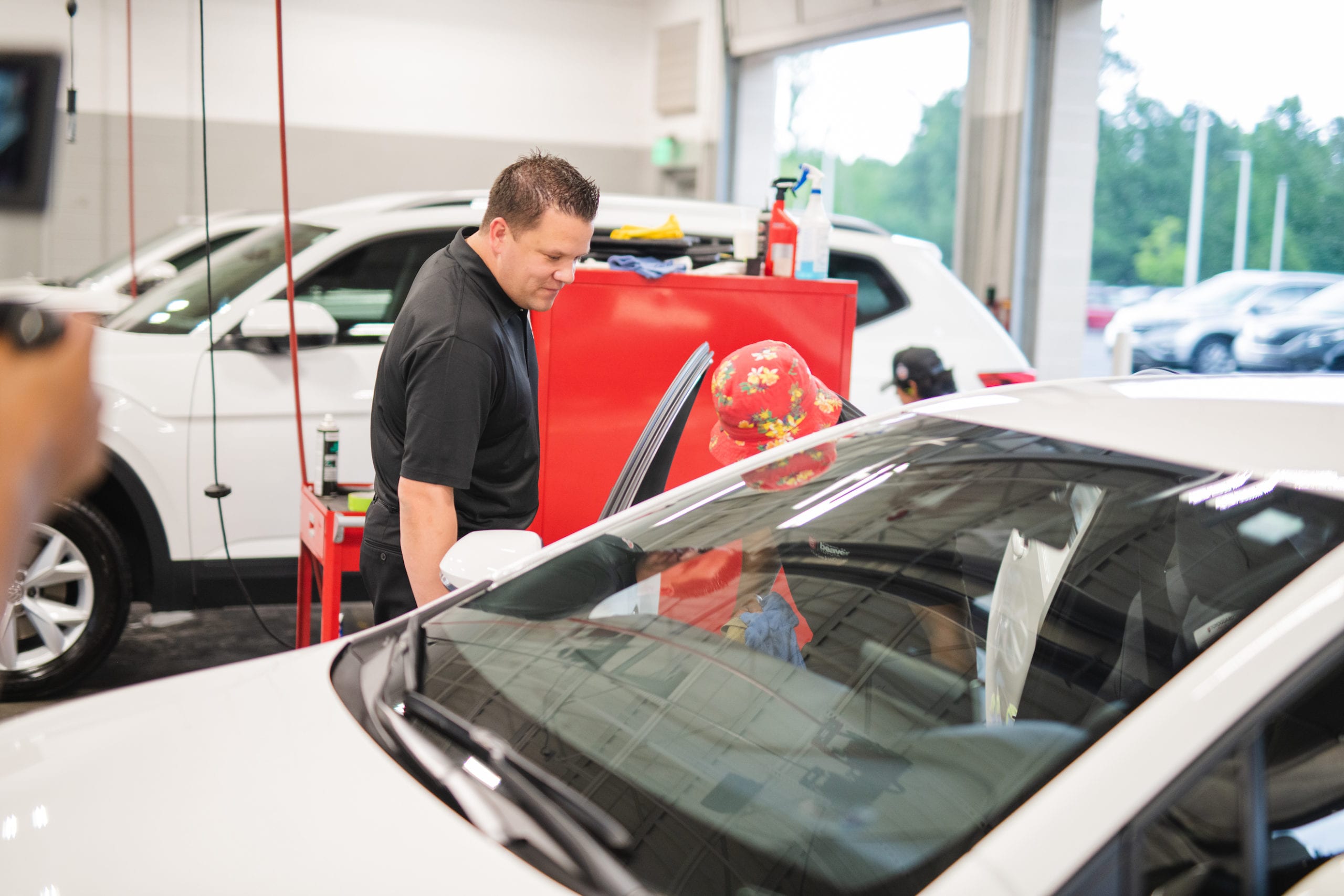 Worker looking on at another worker working on the passenger side of a white car in a garage