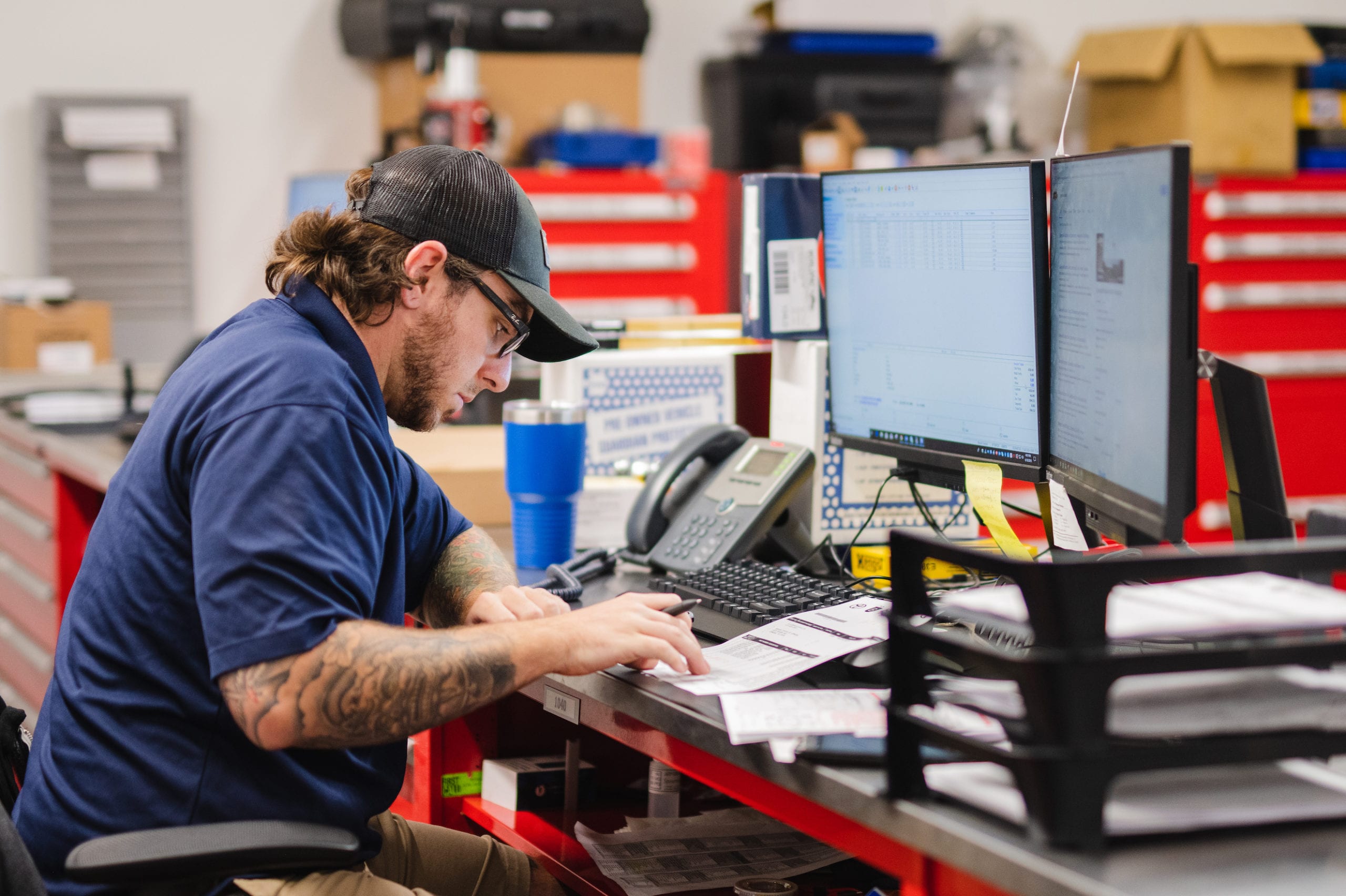 Worker wearing a black cap going through papers by a computer in a garage