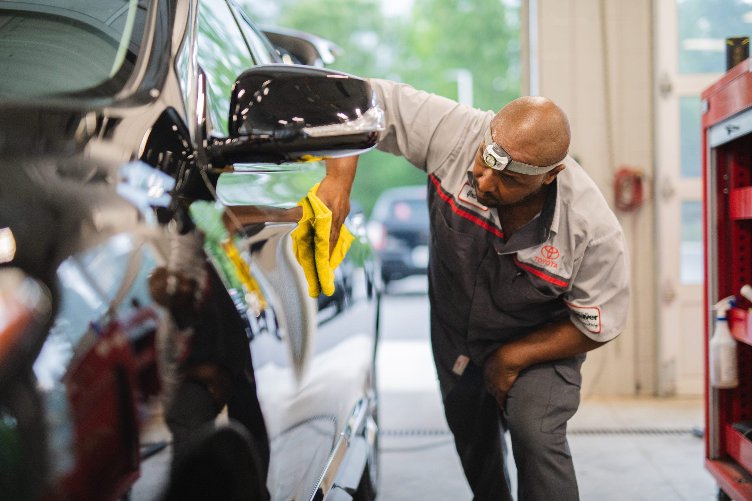 Man polishing the side of a black car with a yellow cloth