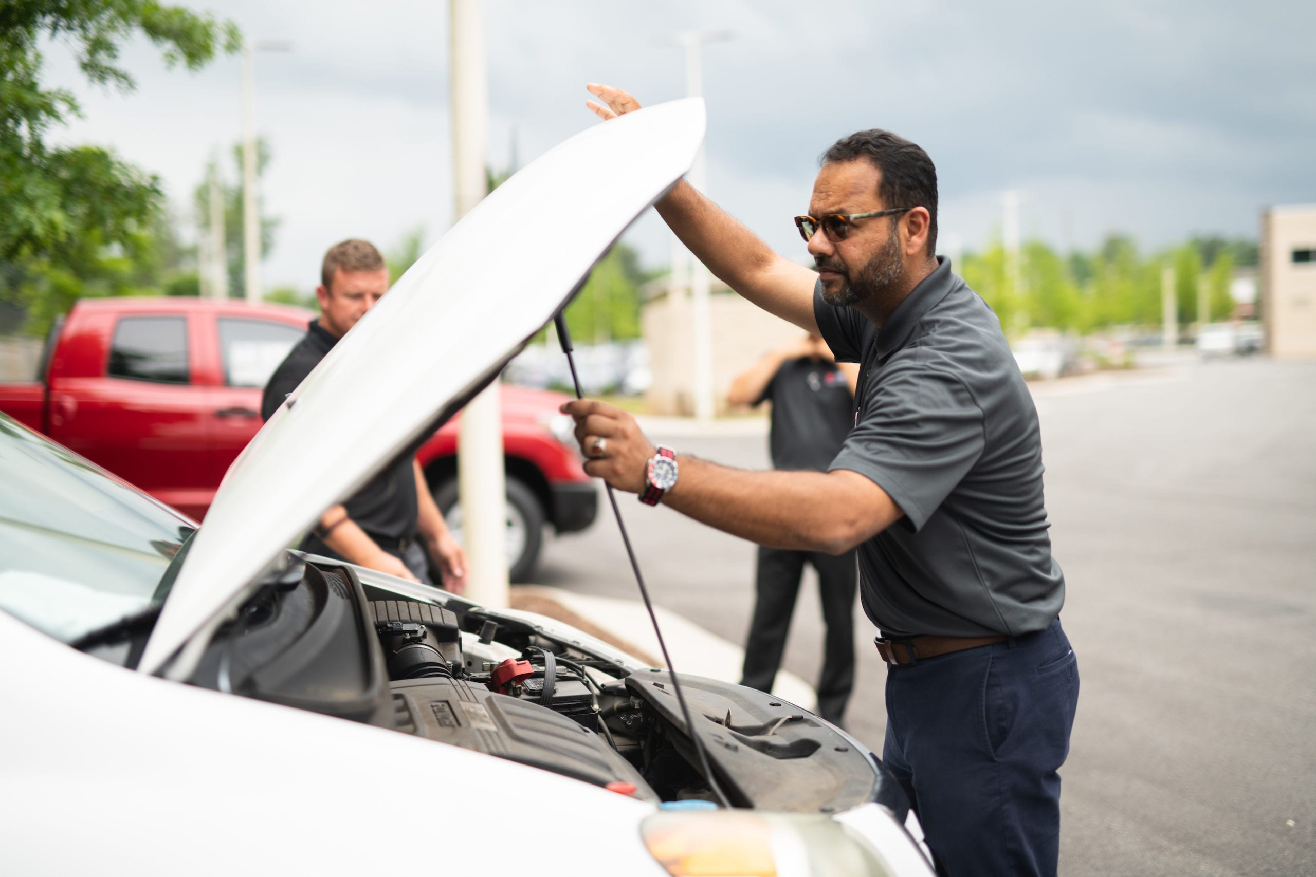 Man working under hood of a white car with two other men in the background