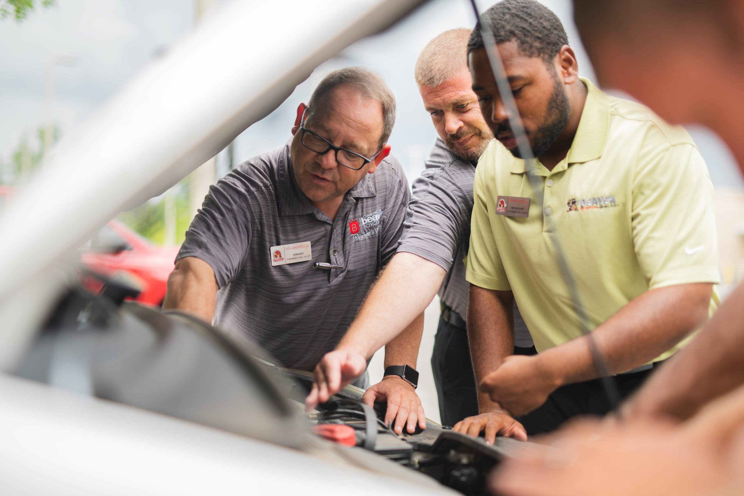 Three men working under a hood of a white car