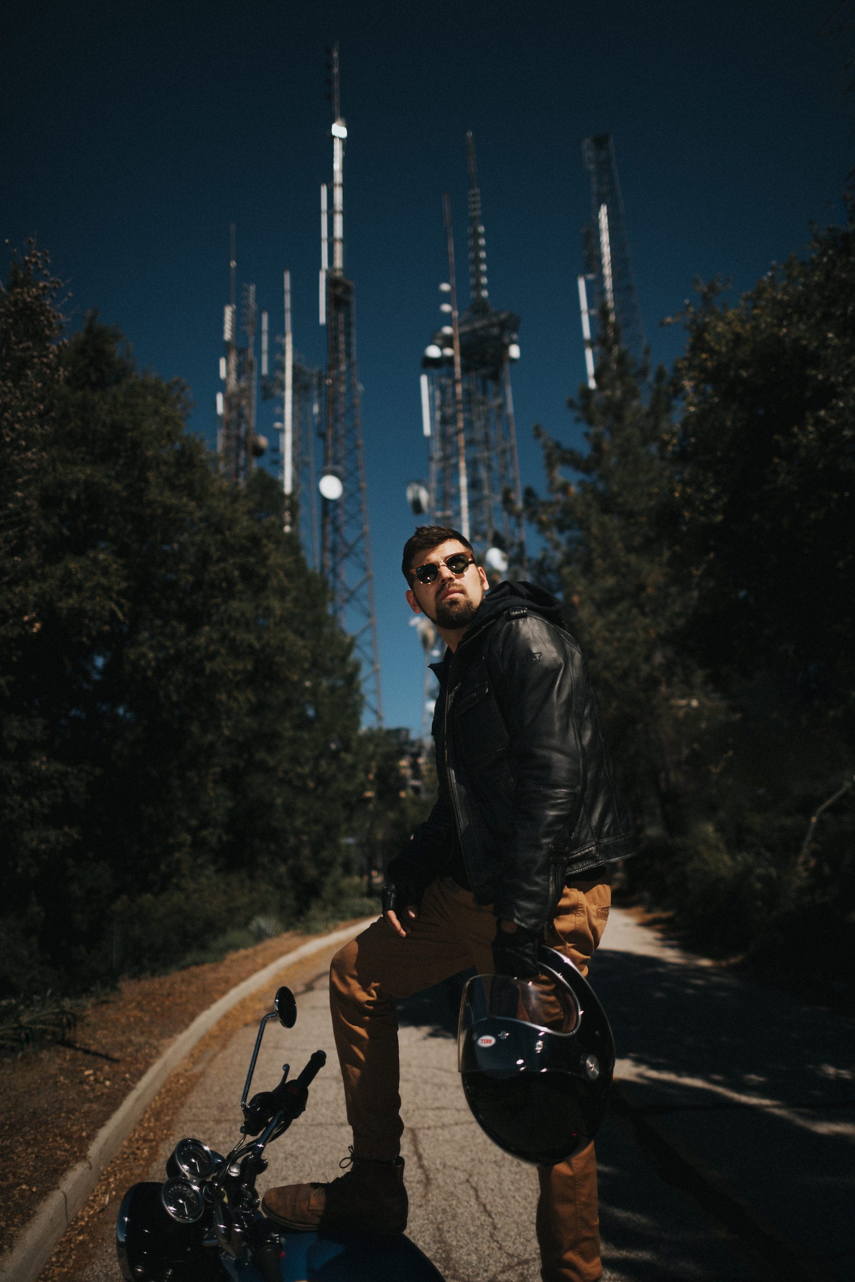 Motorcycle rider standing on top of the Bonneville T100 with large antennae structure dominating the backdrop.