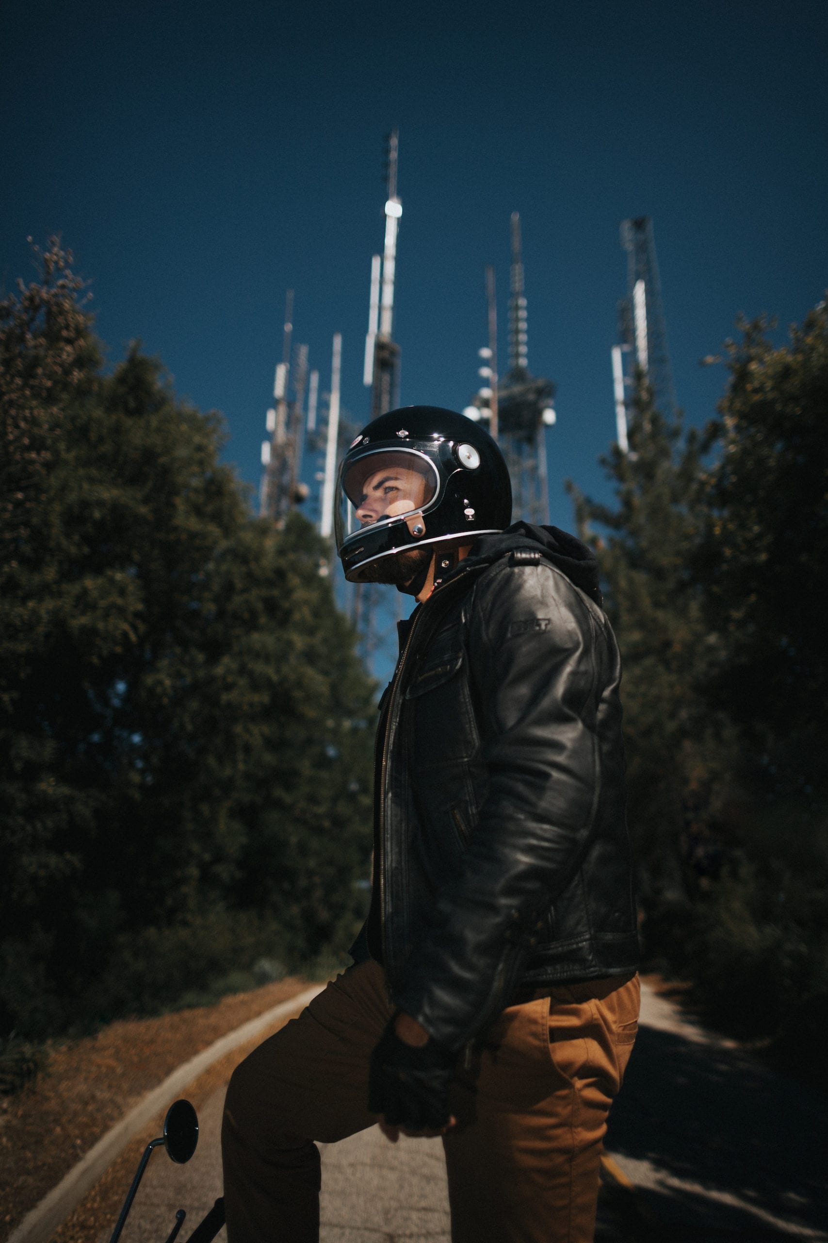 Motorcycle rider standing on top of the Bonneville T100 with large antennae structure dominating the backdrop.