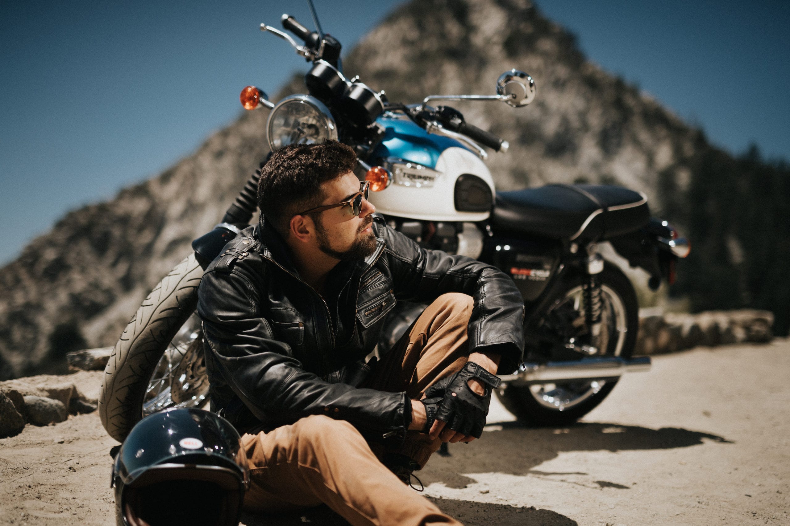 Motorcycle rider resting on the pavement in front of the Bonneville T100 motorcycle with his helmet nearby