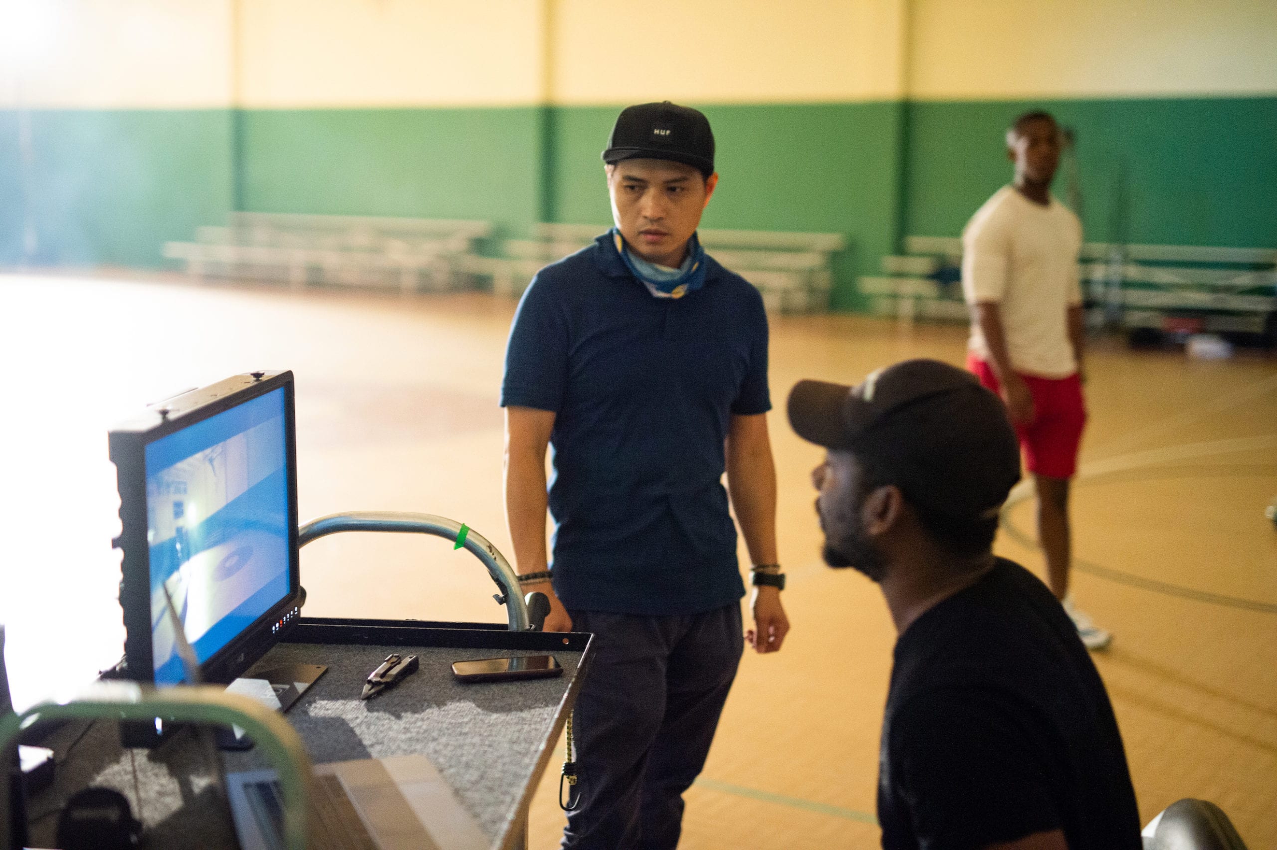Nike African American man checking video equipment on a cart on a basketball court with another crew member looking on