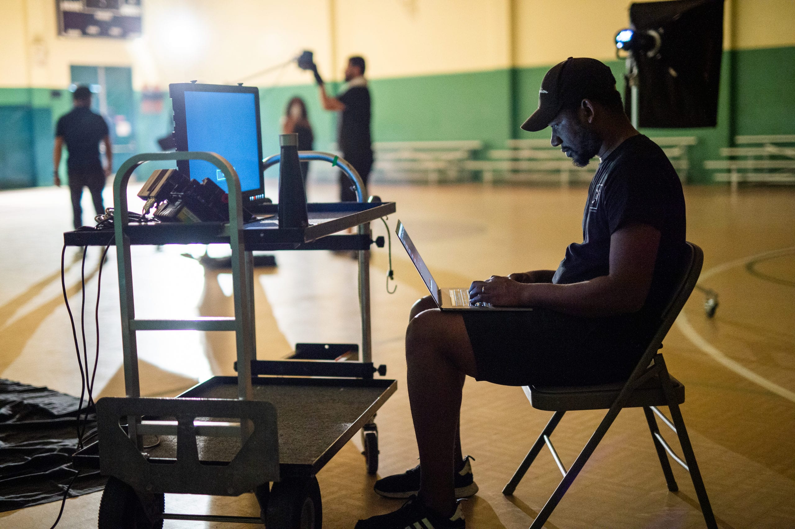 Nike African American man checking laptop next to a cart of video equipment on a basketball court