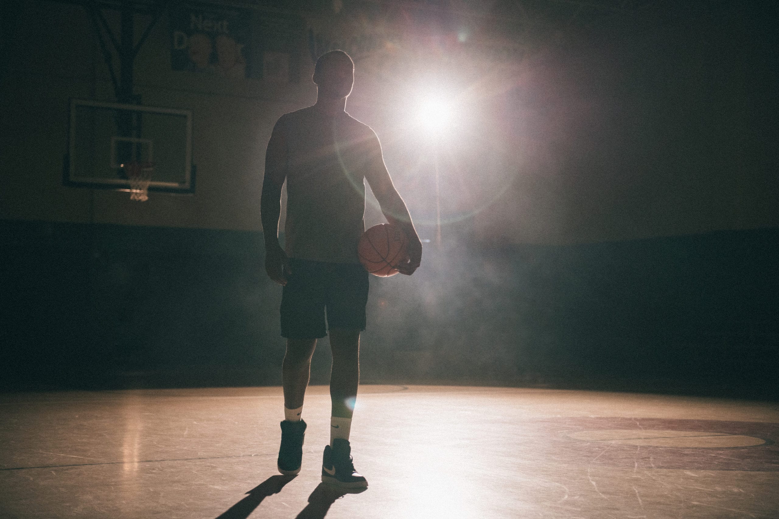 Creative Marketing Concept for Nike Sneakers An African American man holding a basketball on a basketball court with a light shining on him in semi darkness