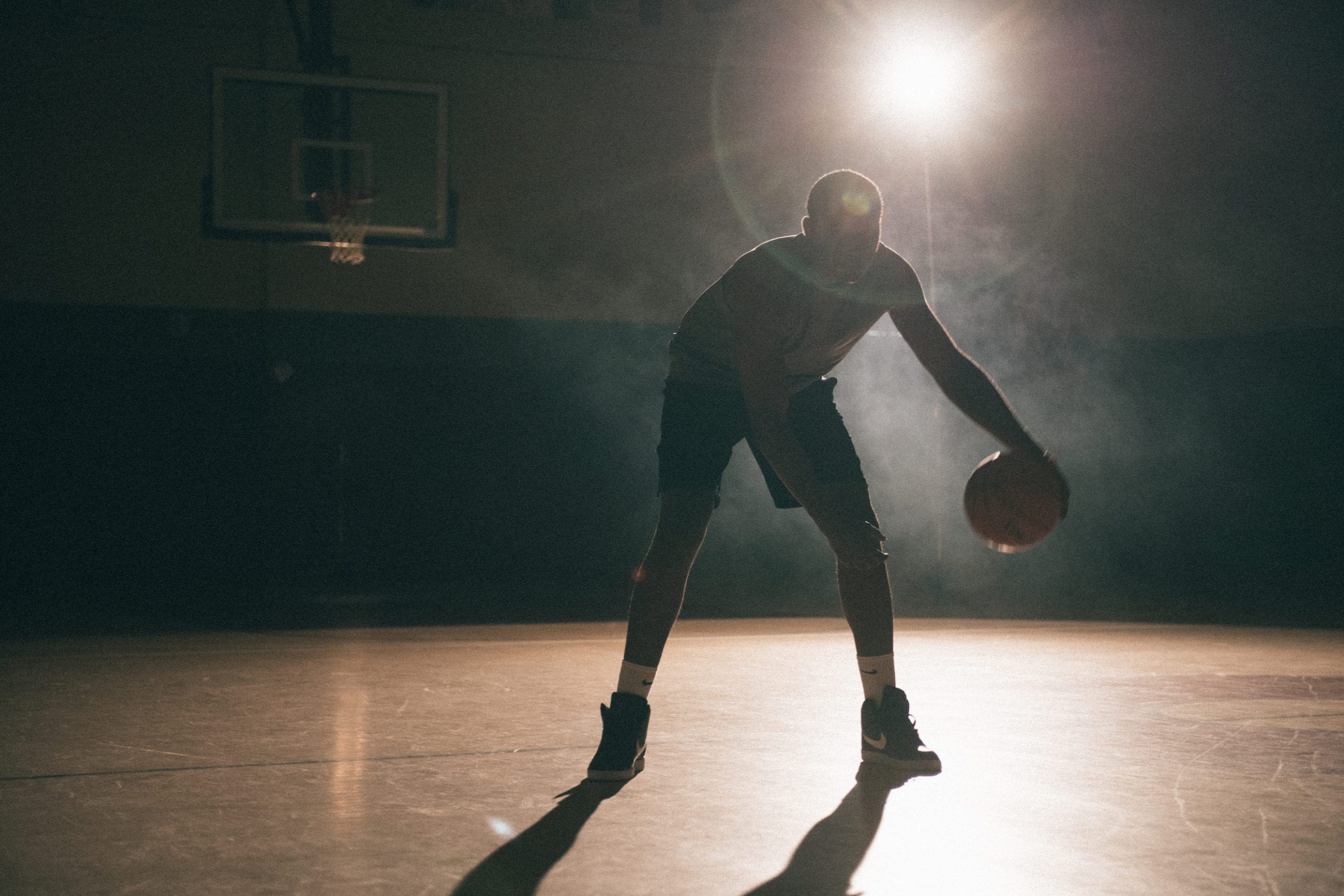 IU C&I Studios PortfolioNike Creative photography An African American man poised holding a basketball on a basketball court with a light shining on him in semi darkness