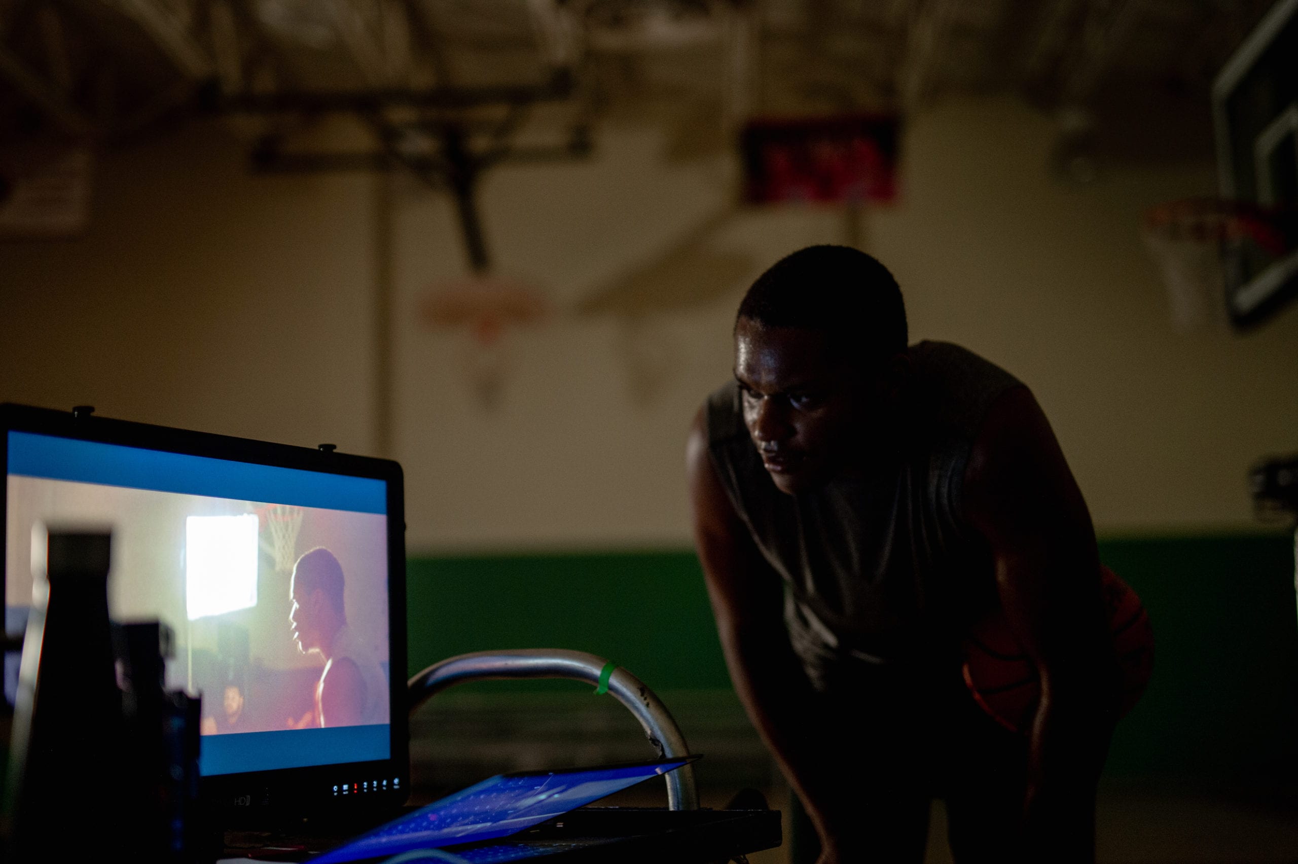 Nike On a basketball court in a gym with an African American man wearing a gray t shirt holding a ball looking at the video display